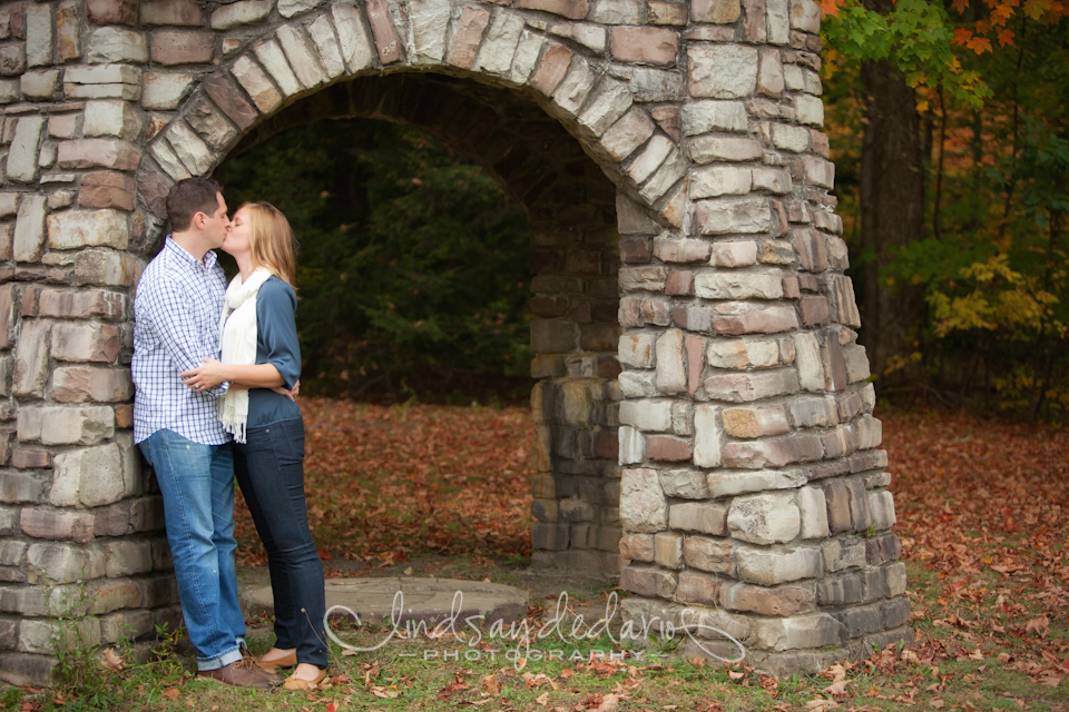 couple kisses under sculpture in Chestnut Ridge Park during their engagement portrait photo in Orchard Park, NY