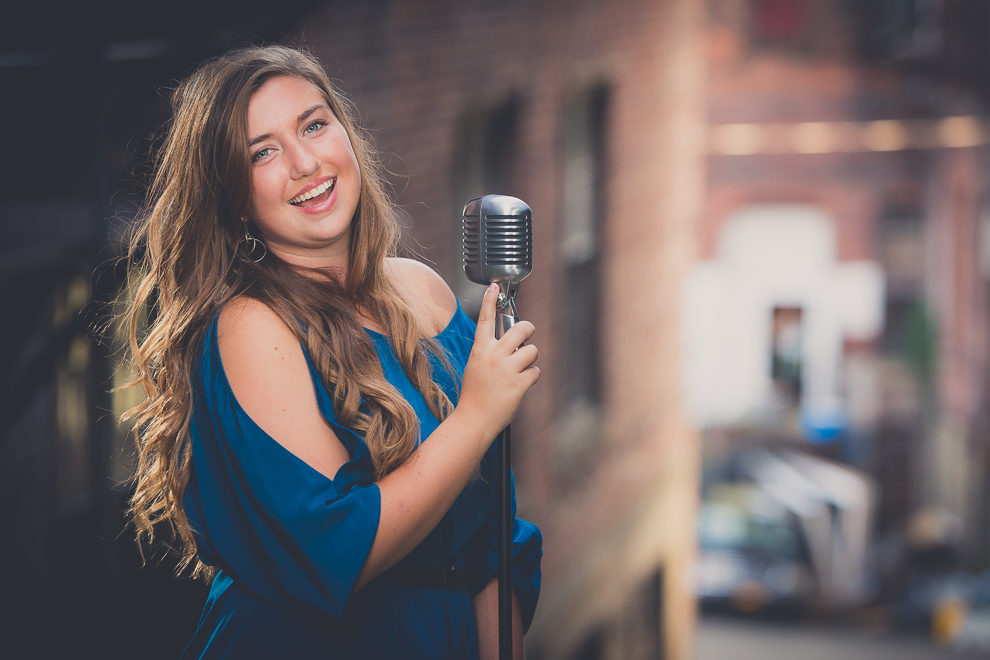 senior portrait photography of young woman smiling with microphone in industrial, edgy looking area of Jamestown, NY, a city in WNY