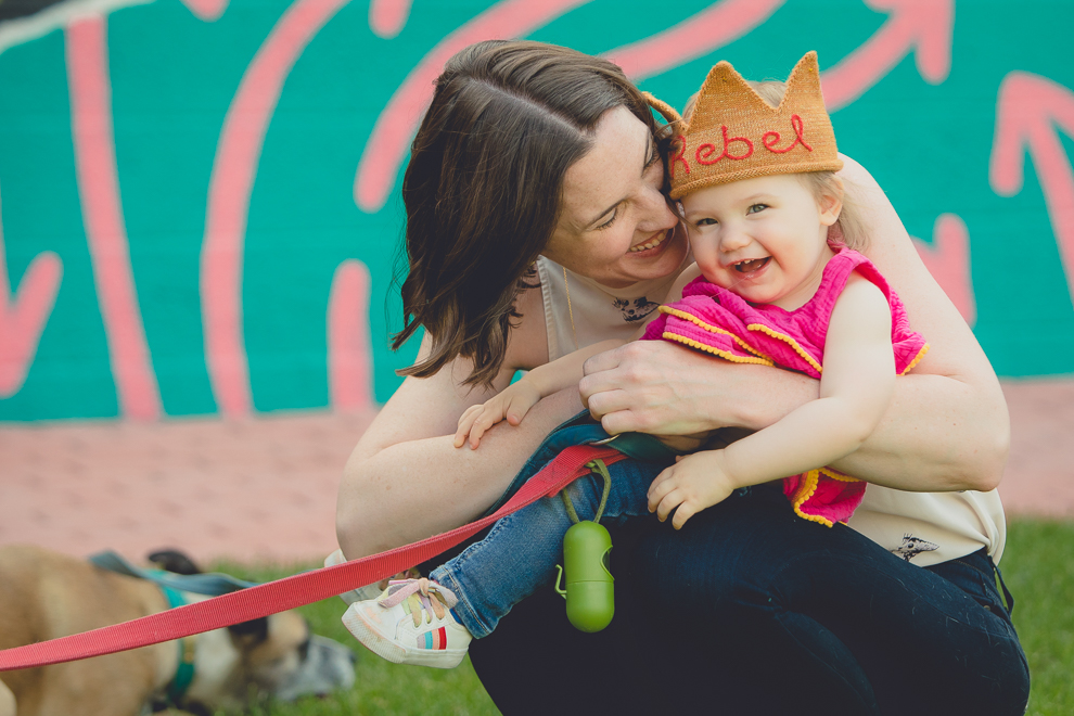 mom tickles daughter during family portrait photography session in front of murals on Chandler St. in Buffalo, NY