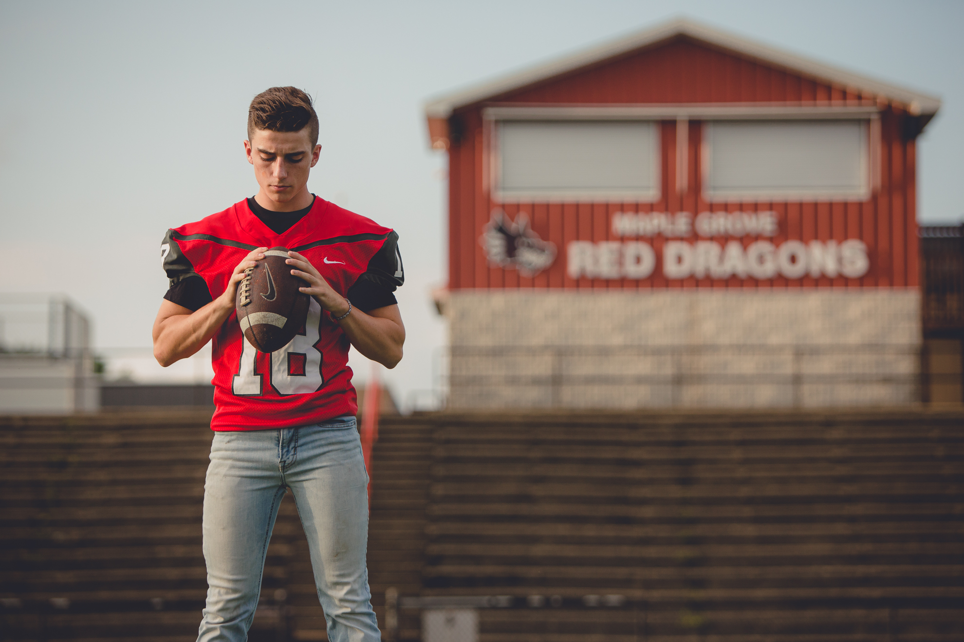 senior picture of football player on field holding ball at Maple Grove high school during portrait session near Buffalo, NY