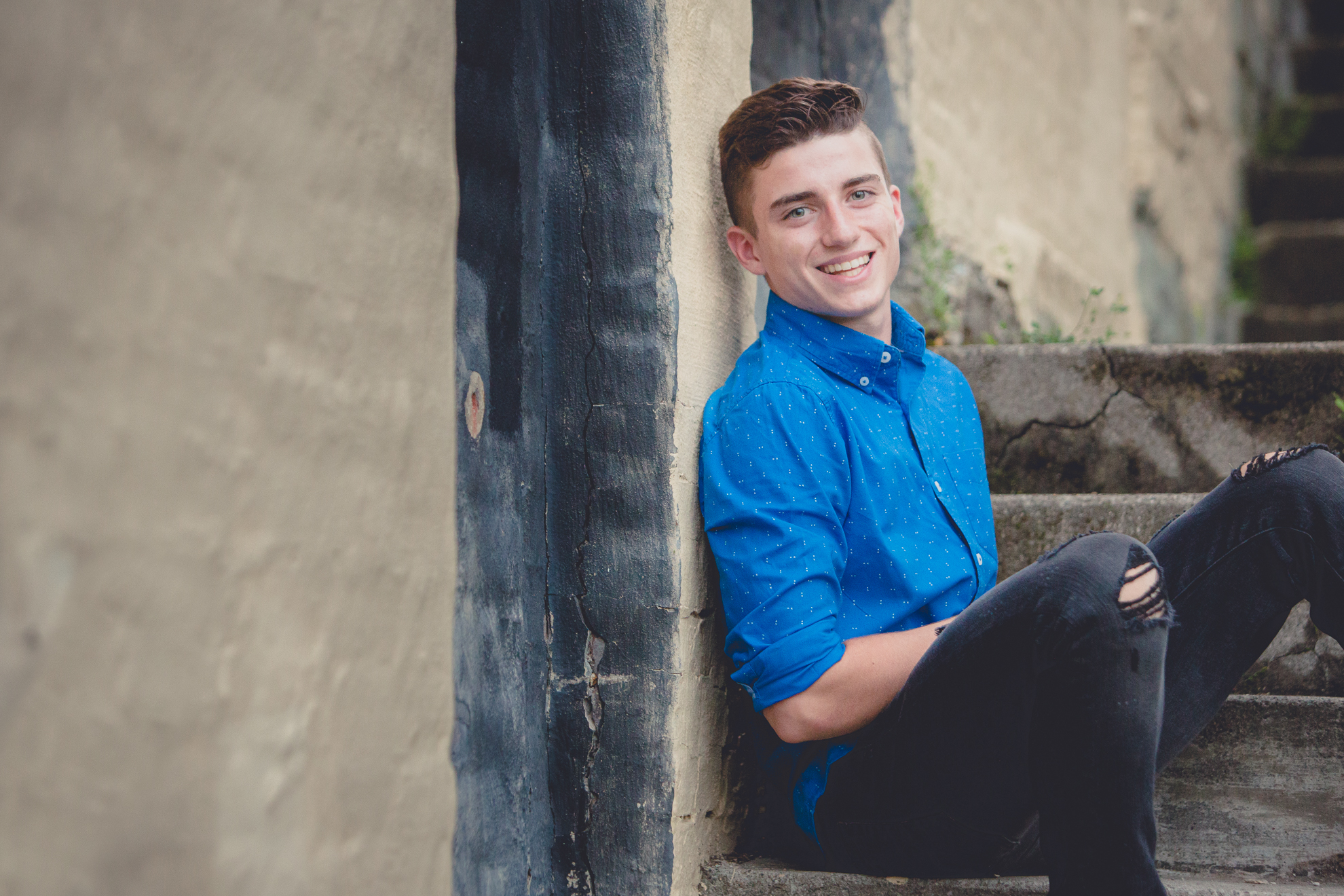 senior portrait of young man leaning on brick wall in Jamestown during photography session 