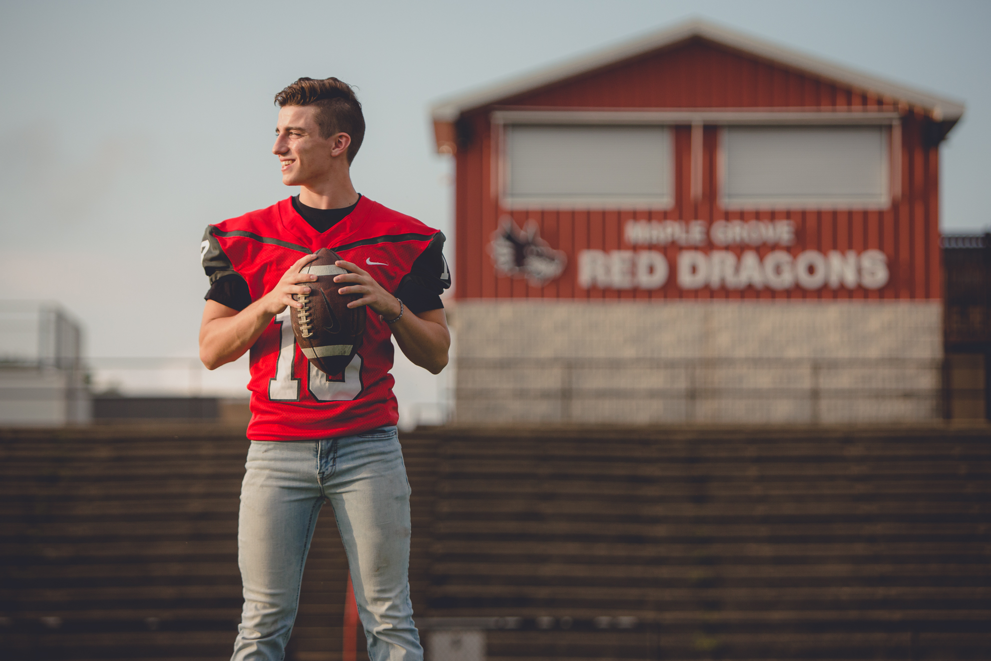 senior picture of football player on field holding ball at Maple Grove high school during portrait session near Buffalo, NY
