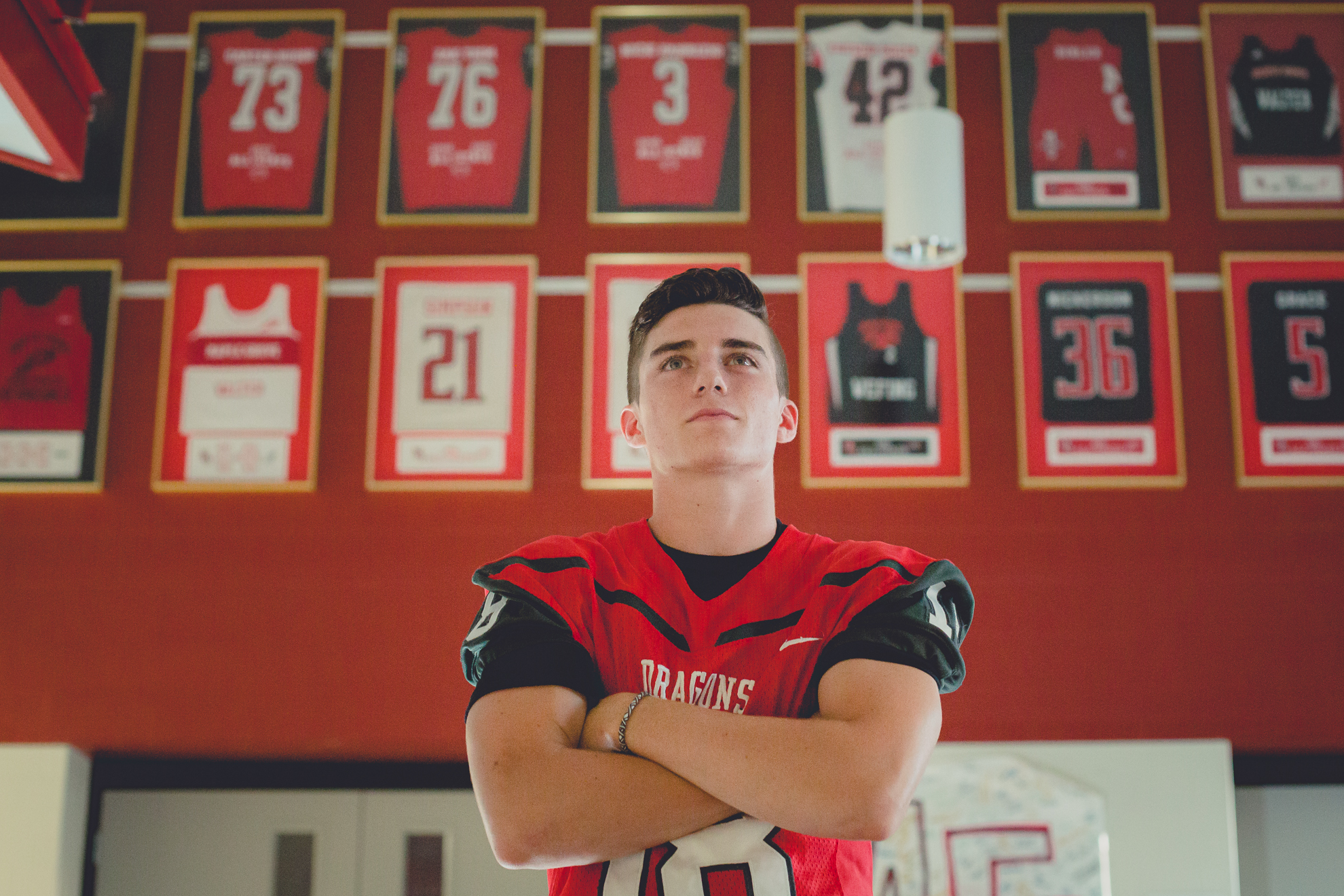 senior football player standing in front of jerseys in school at Maple Grove high school during portrait session near Buffalo, NY
