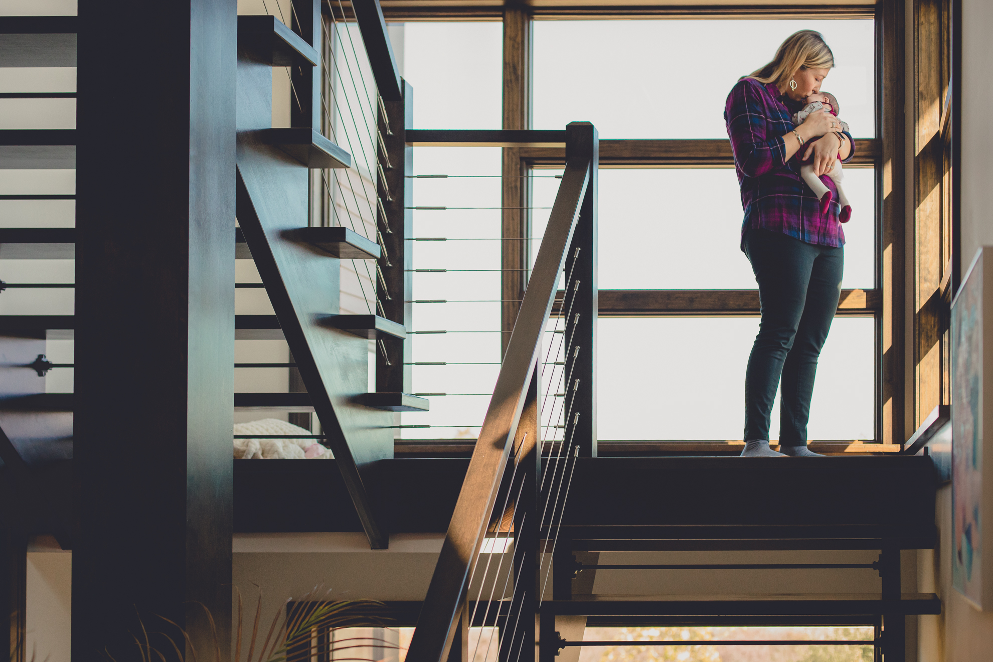 mom holds newborn baby on staircase landing during family portrait photography session in Buffalo, NY