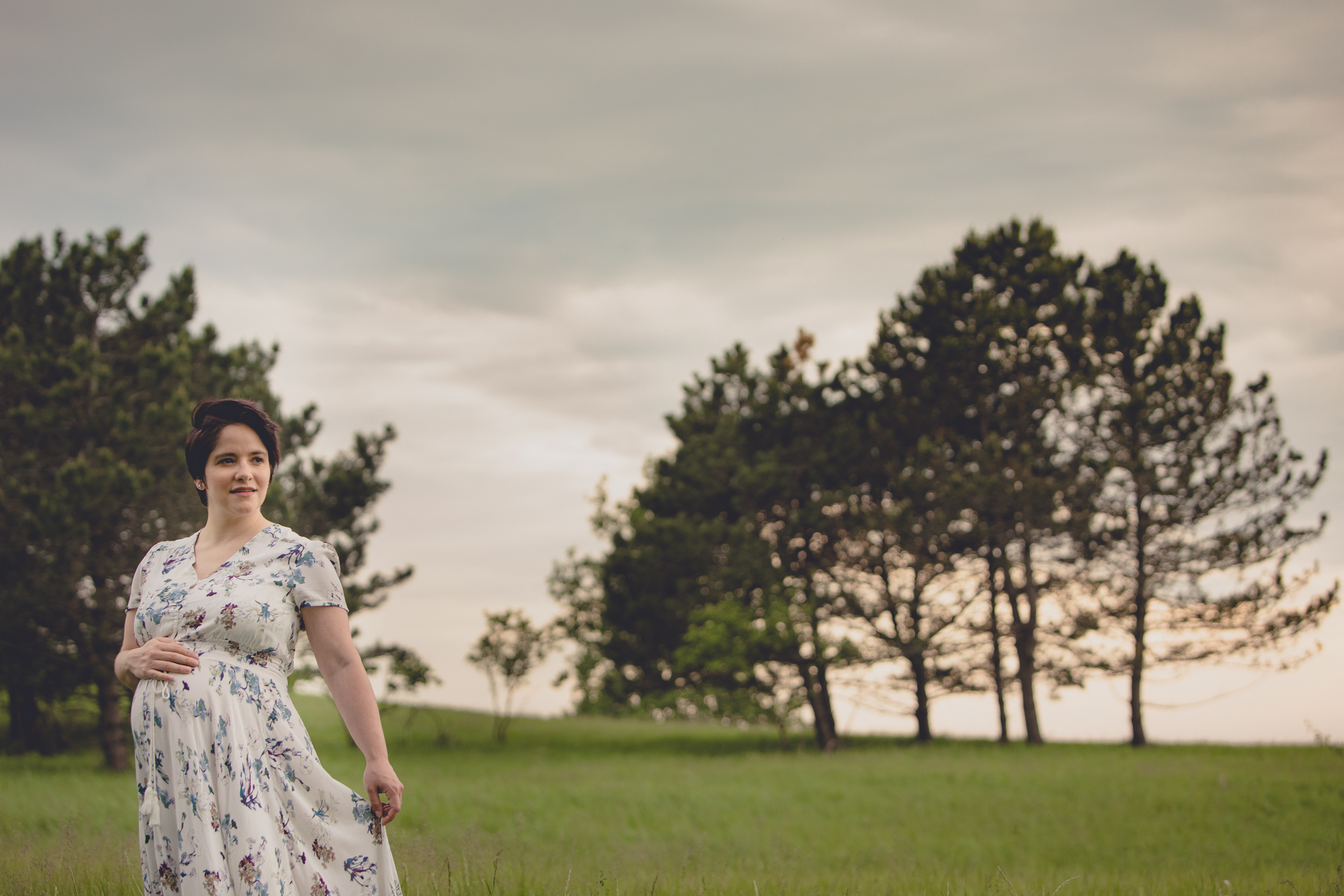 mom looks off to side while holding flowing dress during maternity portrait photography session in field at Tifft Nature Preserve in Buffalo, NY