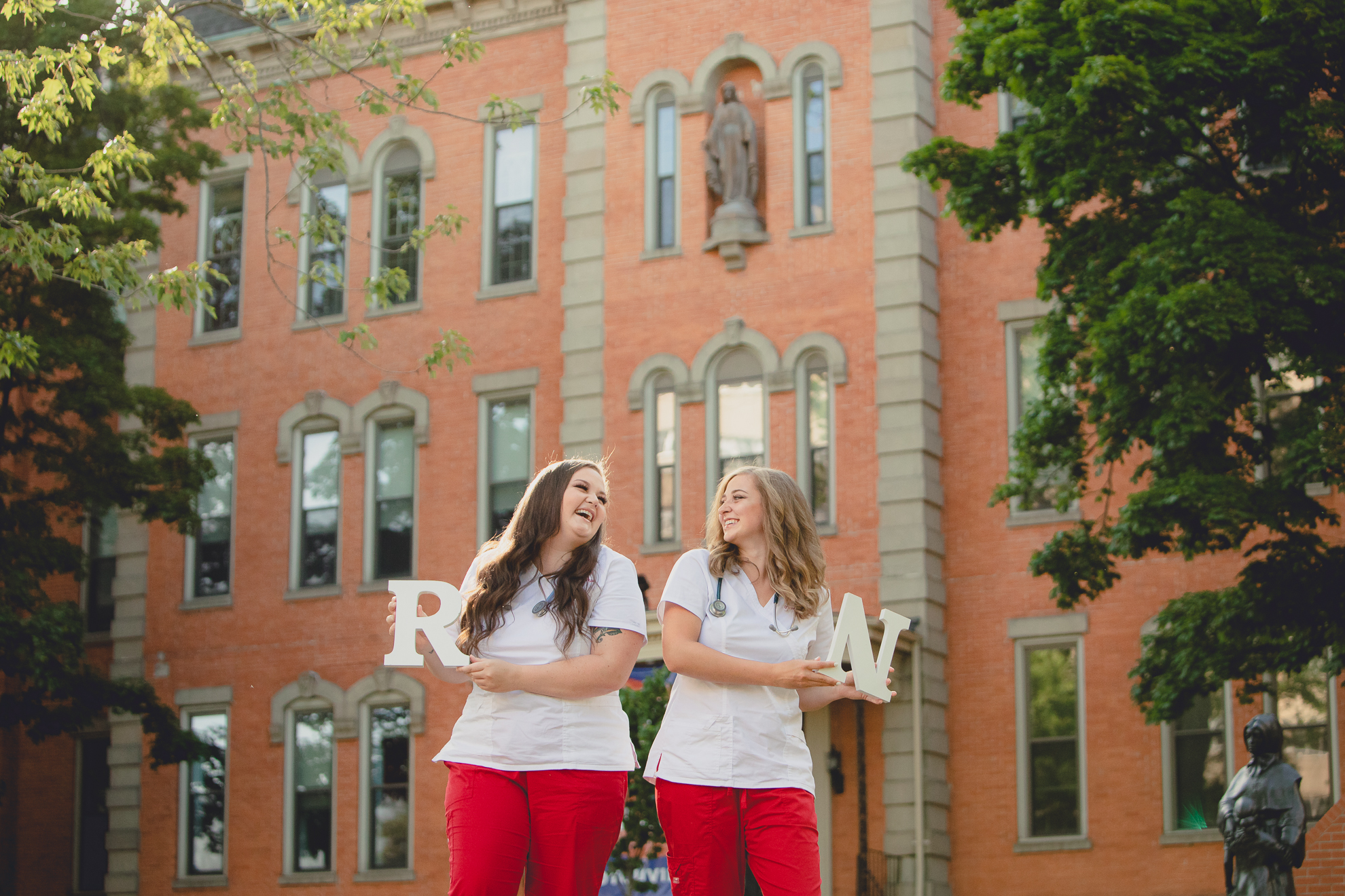 D'youville nursing students hold sign and laugh during senior graduation portrait photography session in Buffalo, NY