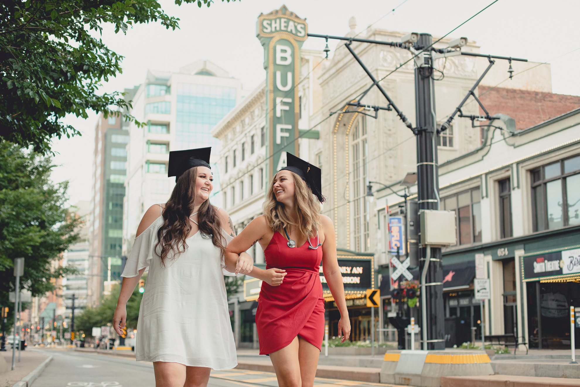 D'youville nursing students walk together laughing in front of Shea's Theater sign during senior portrait photography in Buffalo, NY
