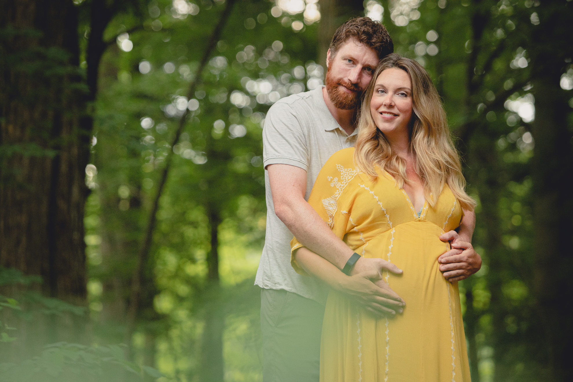 maternity portrait of pregnant mother with husband smiling for photographer in forest at Chestnut Ridge Park near Buffalo, NY