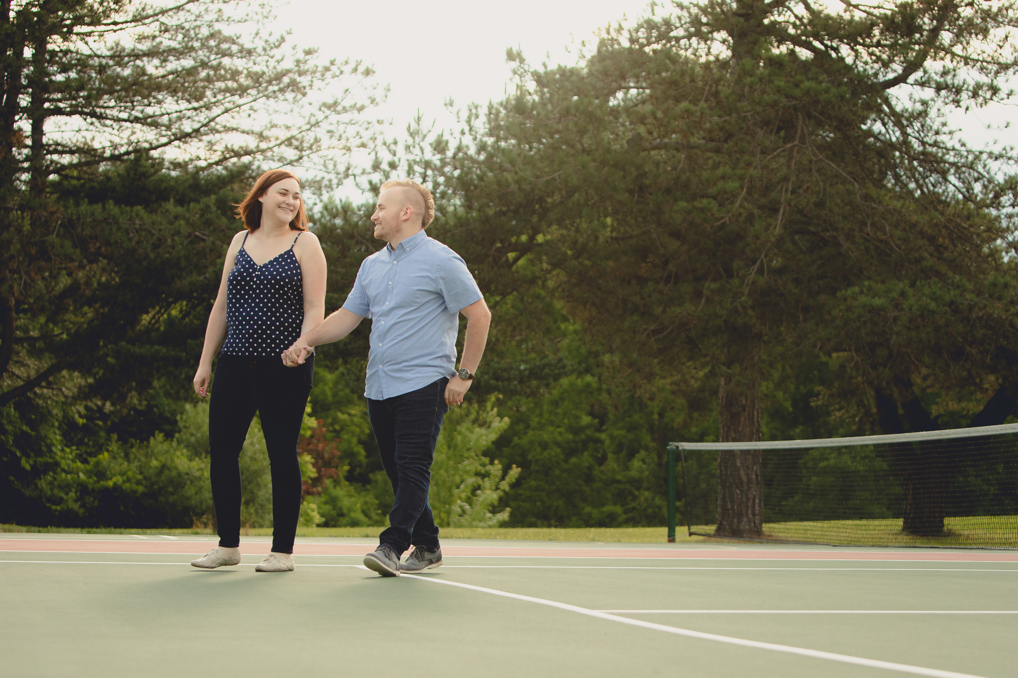 engaged couple walks together on tennis court at Akron Falls Park near Buffalo, NY