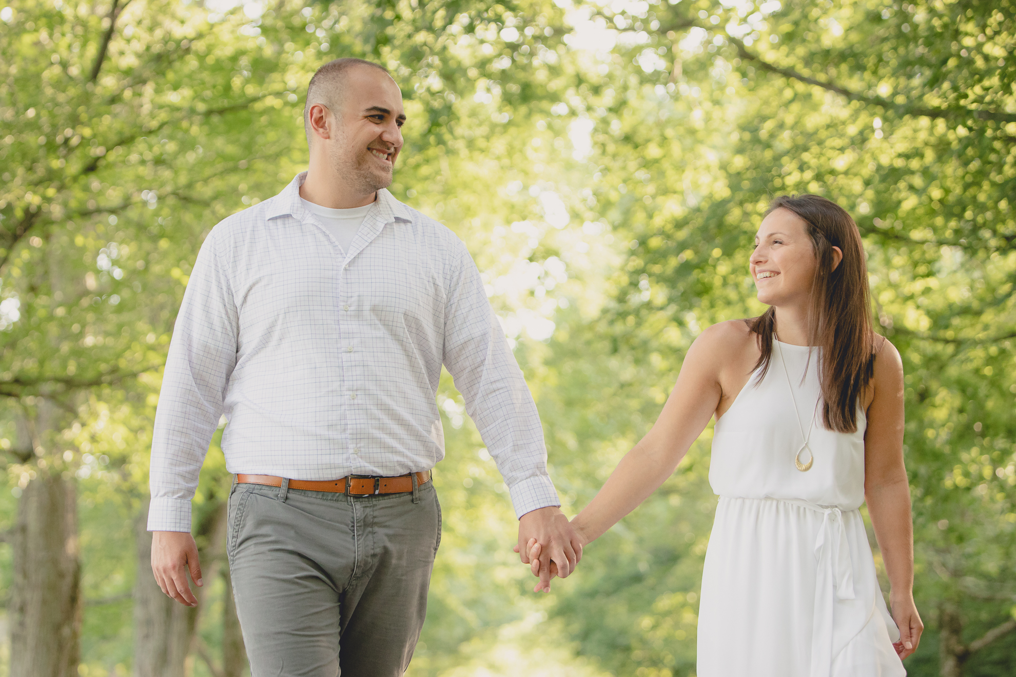 bride and groom laugh and hold hands while walking down tree lined road during wedding photography engagement portrait session at Knox Farm near Buffalo, NY