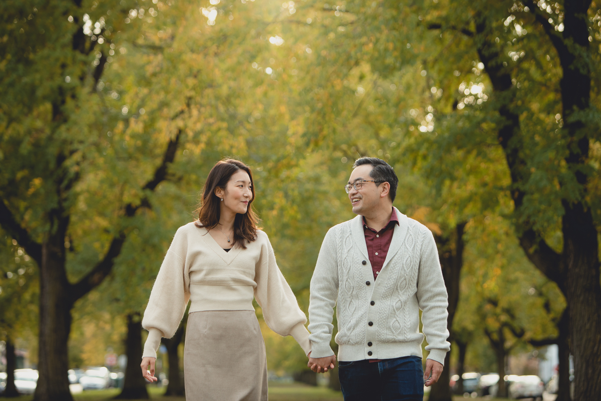 bride and groom walk holding hands during engagement photography session among fall foliage in Bidwell Parkway in Buffalo, NY