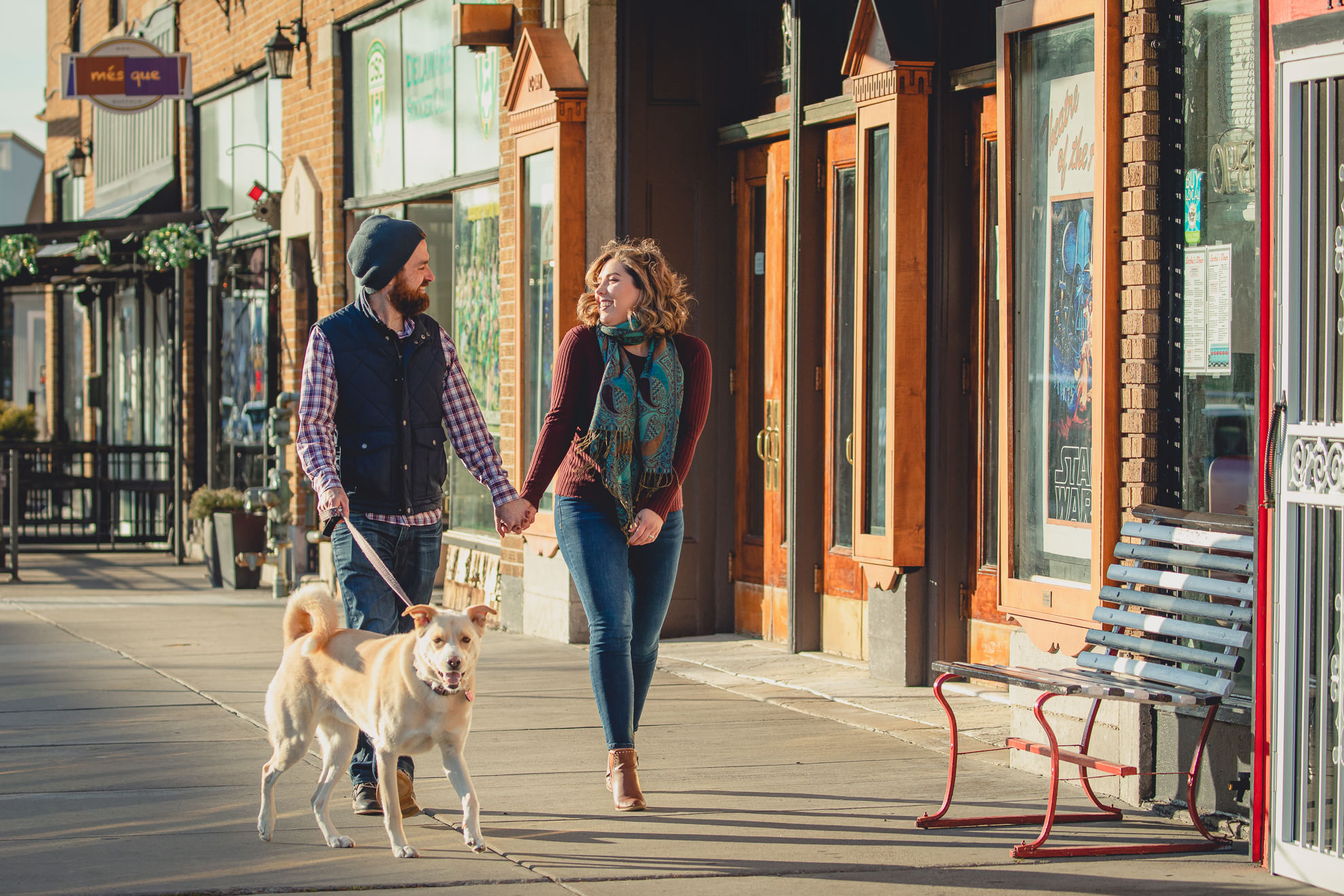 couple walks dog in front of North Park Theater during couples mini photography session on Hertel Ave. in North Buffalo, NY