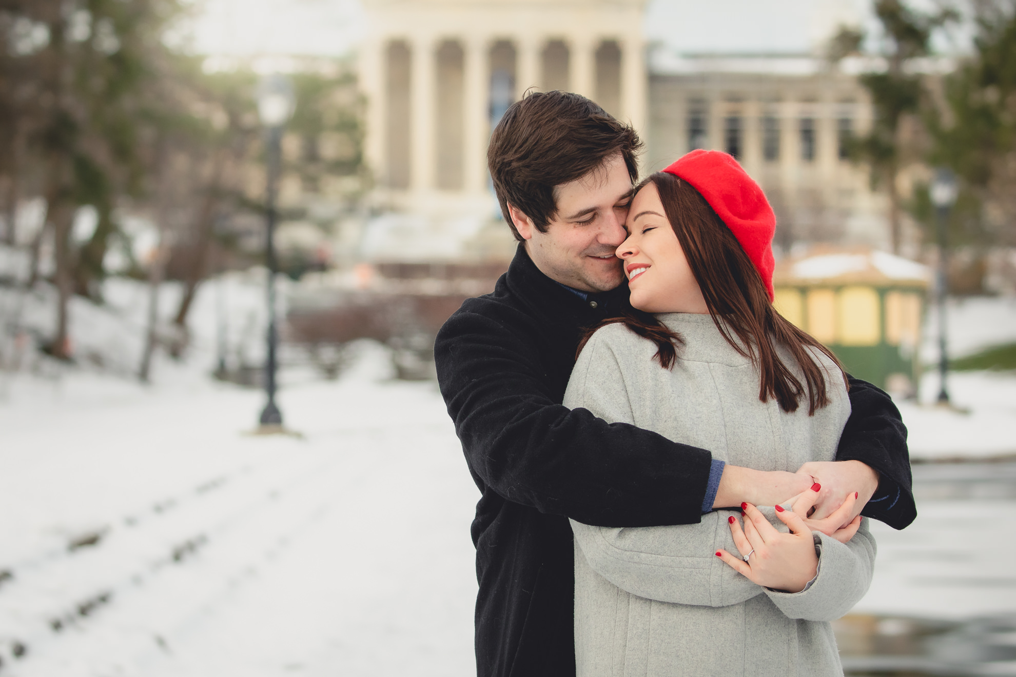 groom kisses bride on cheek next to Hoyt Lake with Albright Knox Art Gallery in the background during their wedding engagement photography session in Buffalo, NY