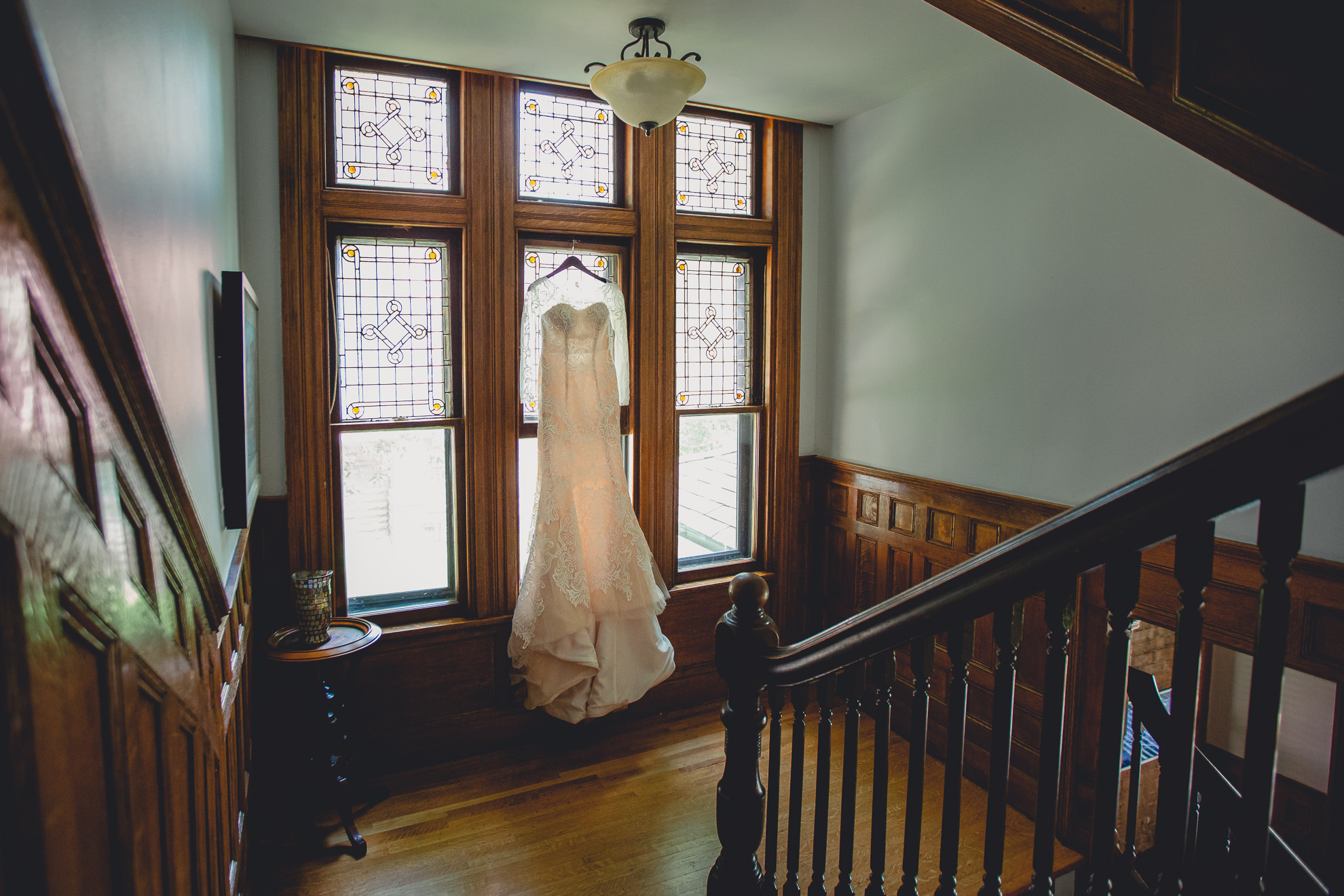 brides dress hangs in stained glass window at Strathallan Hotel in Rochester, NY before wedding