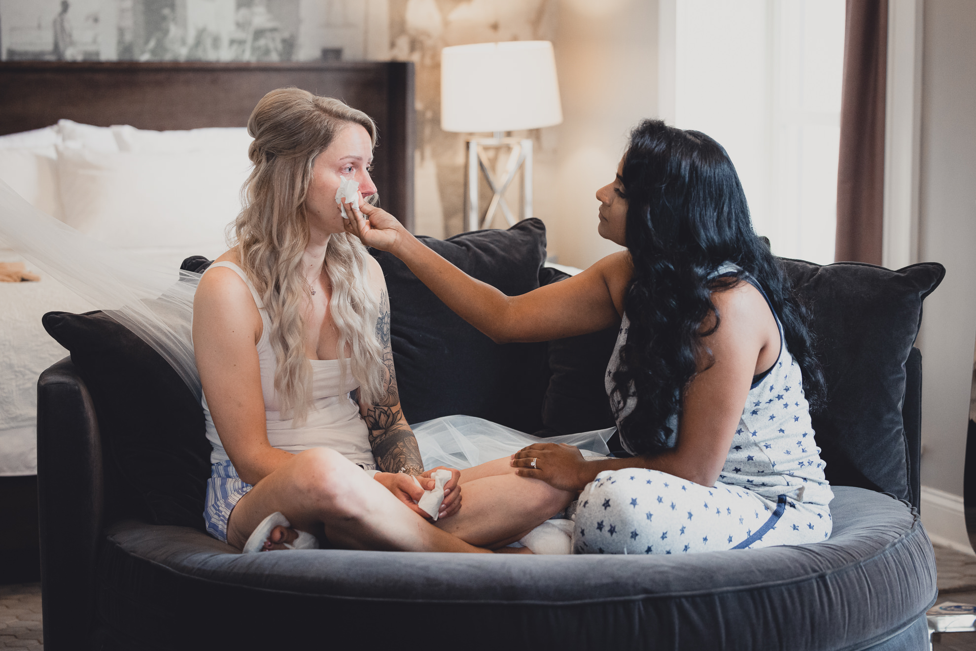 bride and bridesmaid chat on sofa while getting ready for wedding at Hotel Lafayette in Buffalo, NY