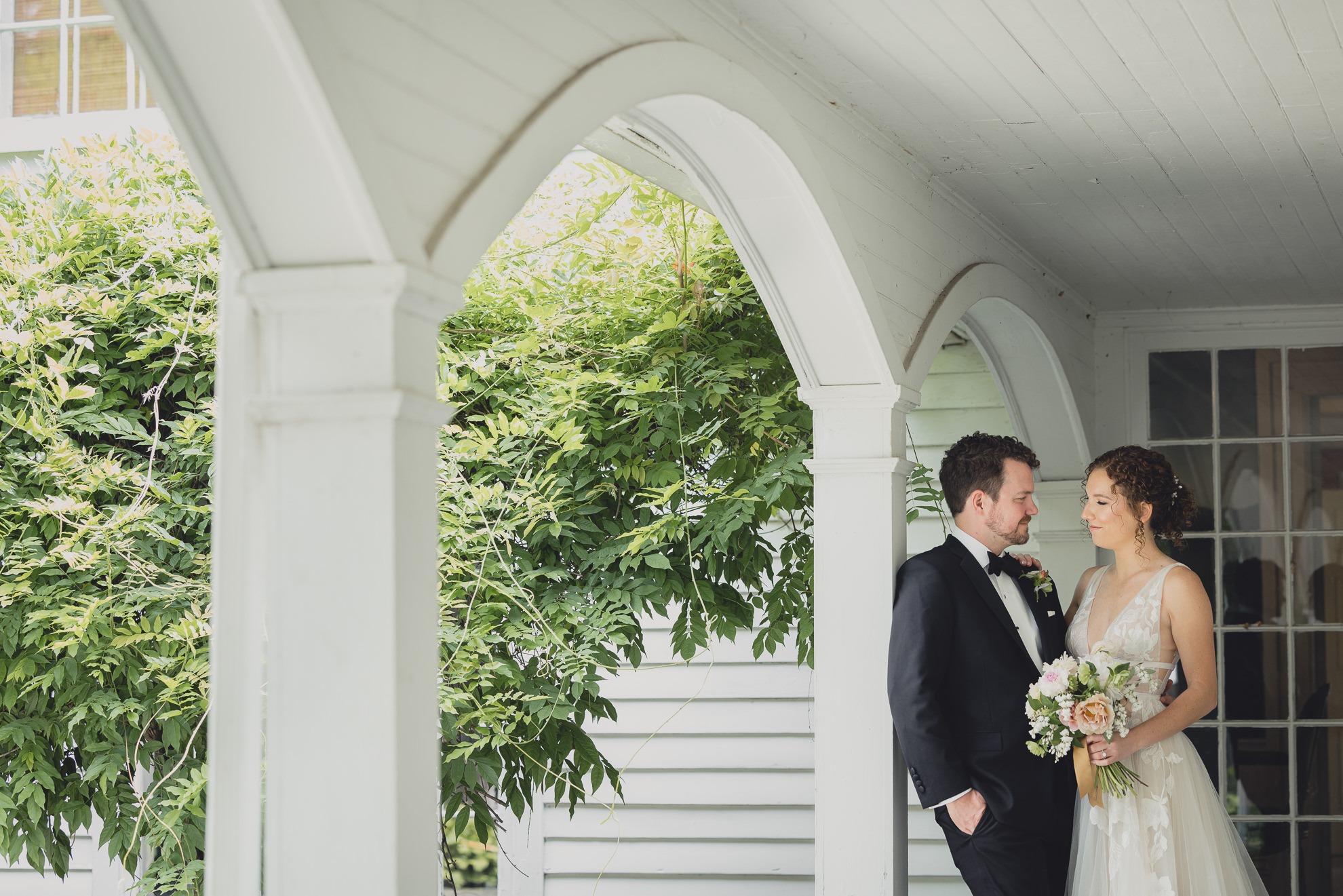 bride and groom look at each other under archway at Barton Hill House in Lewiston, NY before wedding