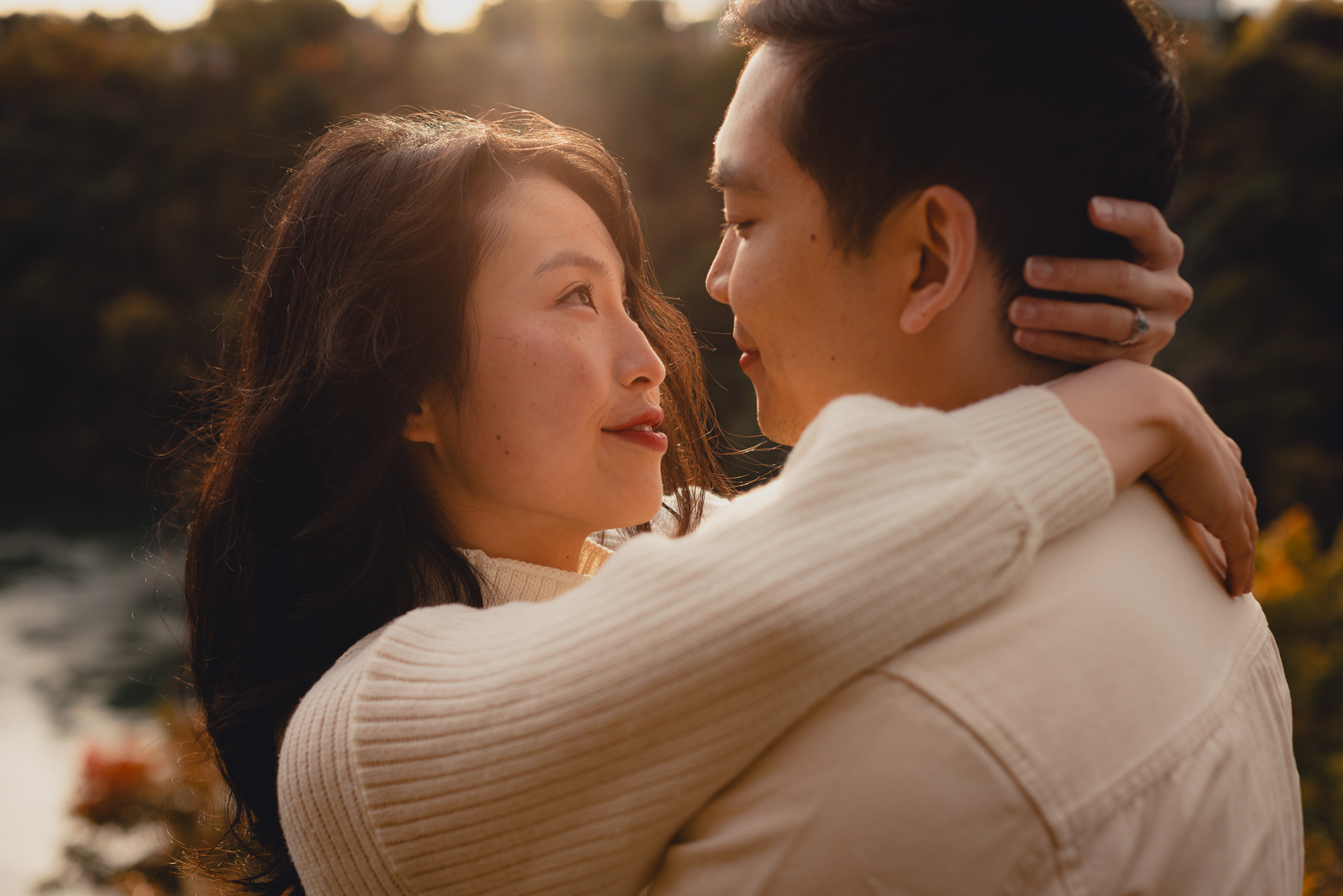 couple looks at each other with fall foliage in background during wedding engagement photography session in Niagara Falls, NY