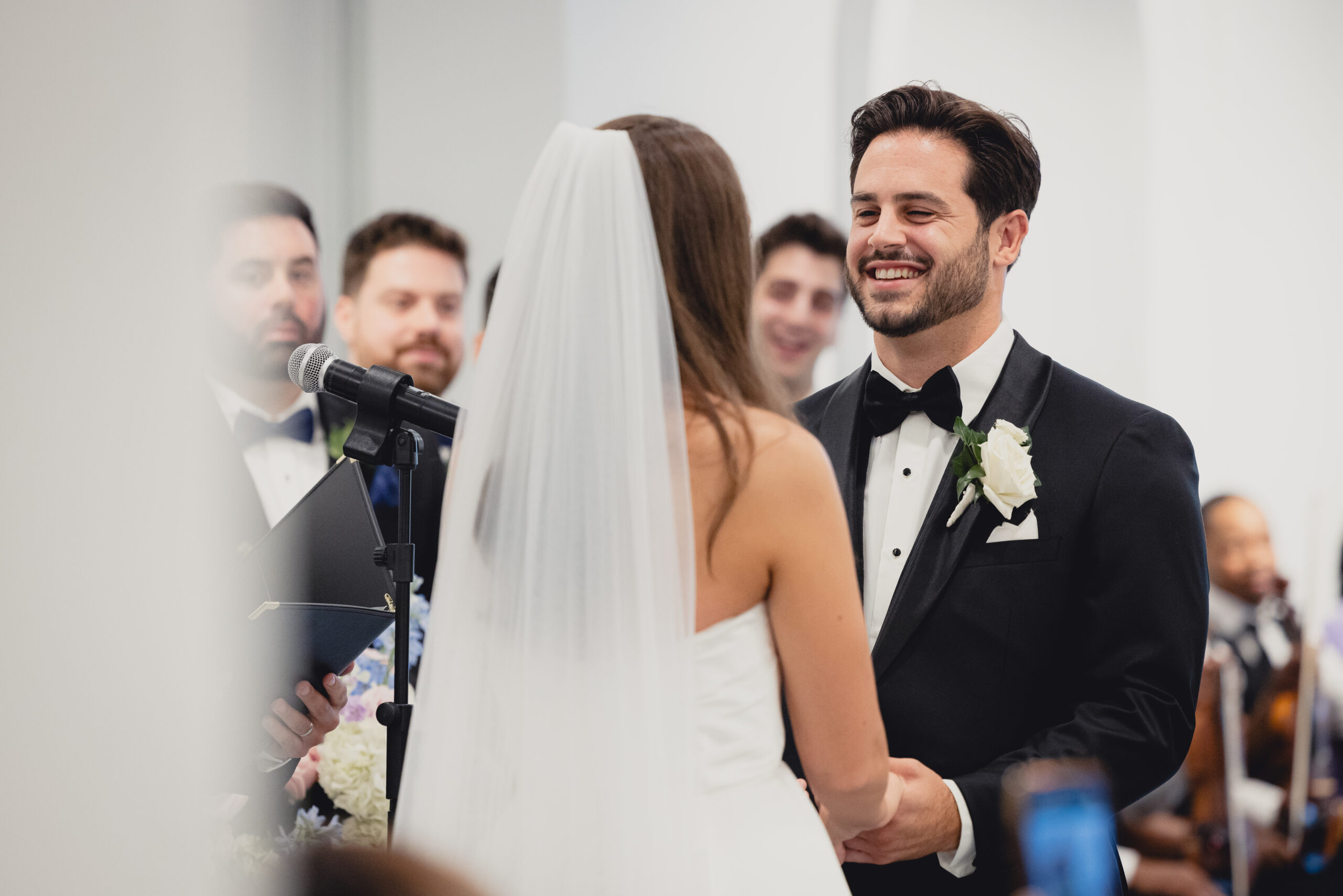groom smiles at bride during wedding ceremony in the Portico Gallery of the Buffalo History Museum