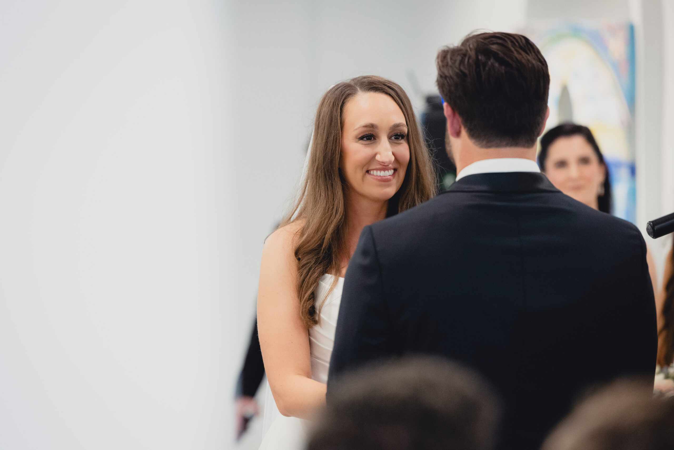 bride smiles at groom during wedding ceremony in the Portico Gallery of the Buffalo History Museum