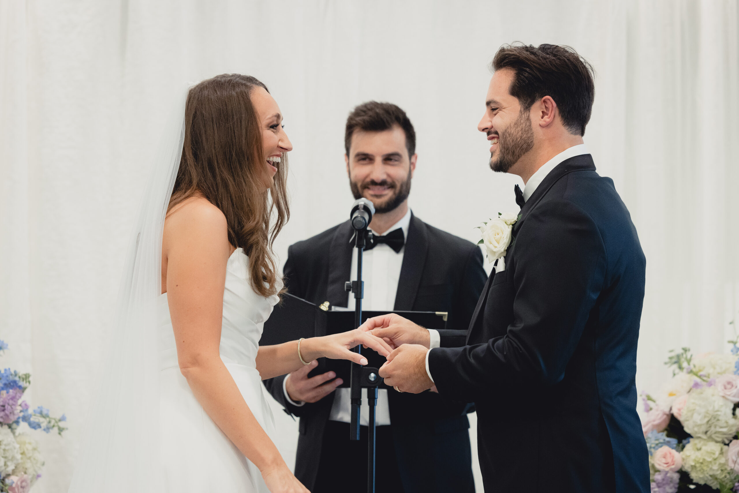 groom puts ring on bride during wedding ceremony in the Portico Gallery of the Buffalo History Museum