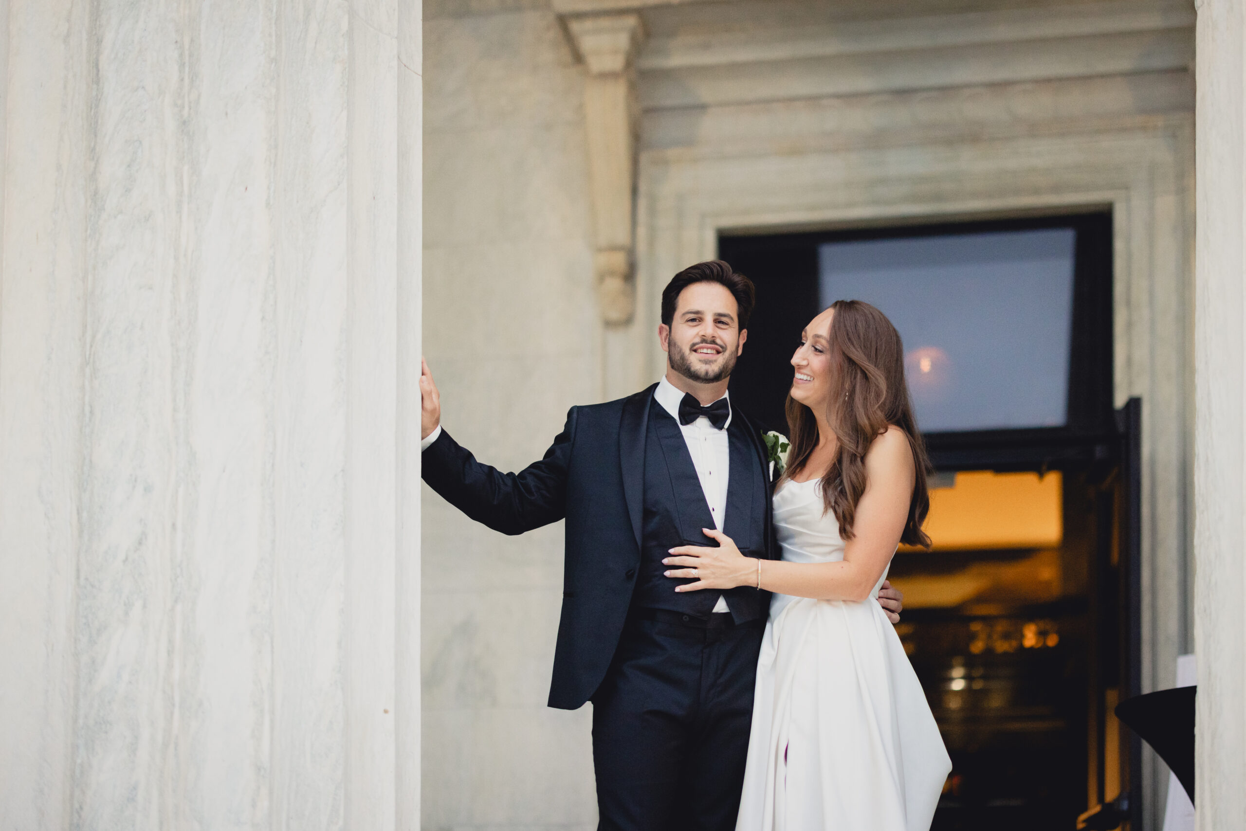 bride and groom look out from portico during wedding reception at the Buffalo History Museum