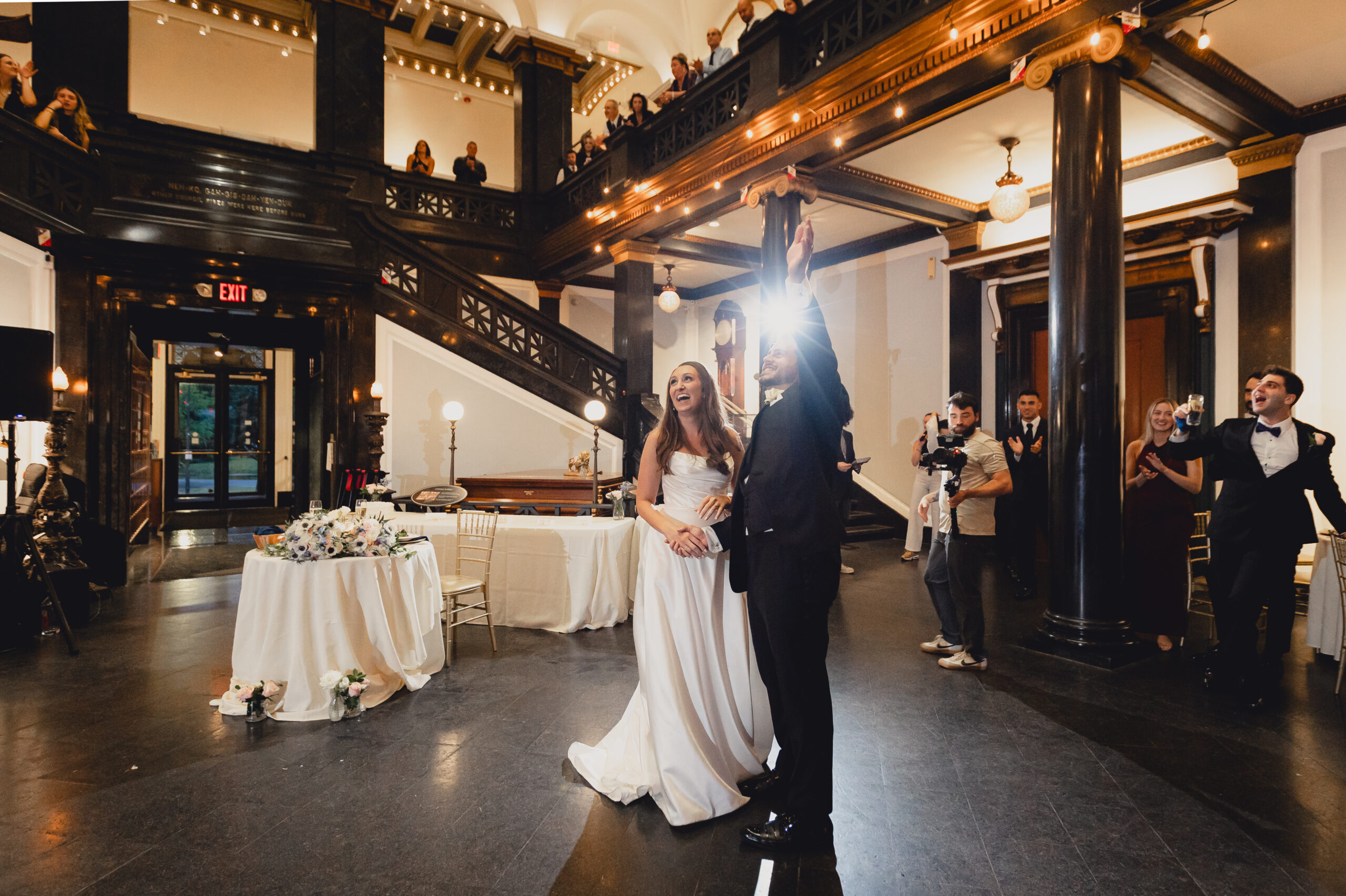 groom waves to guests on mezzanine level during entrances during wedding reception at the Buffalo History Museum