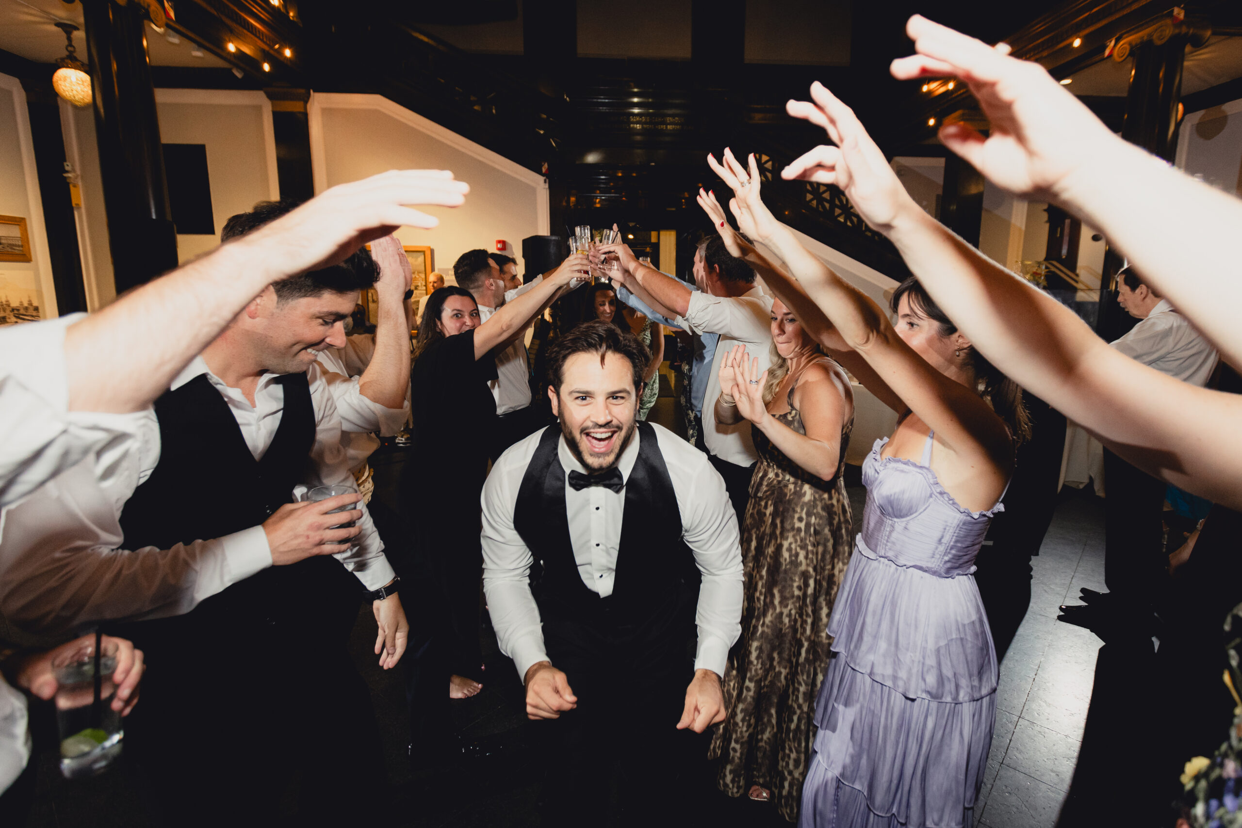 groom walks under guests outstretched arms during wedding reception at the Buffalo History Museum