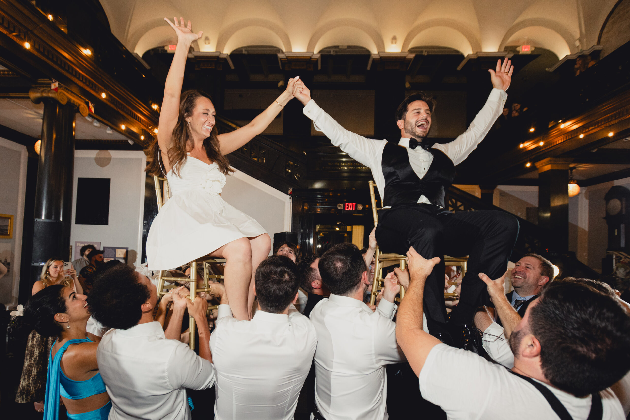 bride and groom seen on chairs held up by guests during hava nagila during wedding reception at the Buffalo History Museum