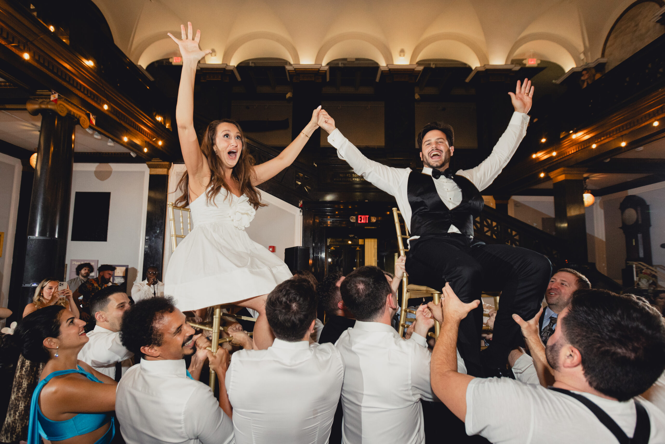bride and groom seen on chairs held up by guests during hava nagila during wedding reception at the Buffalo History Museum