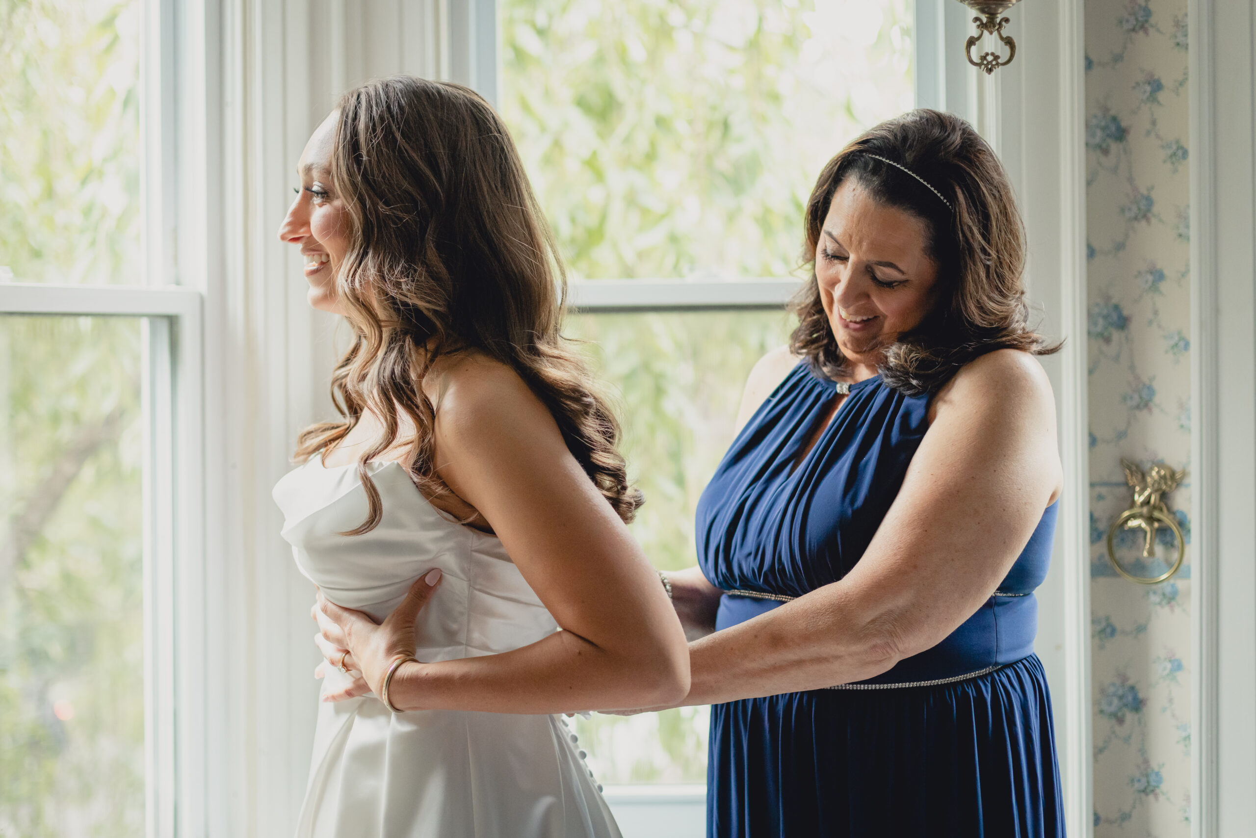 mother helps bride button dress in childhood bedroom before wedding in Buffalo, NY