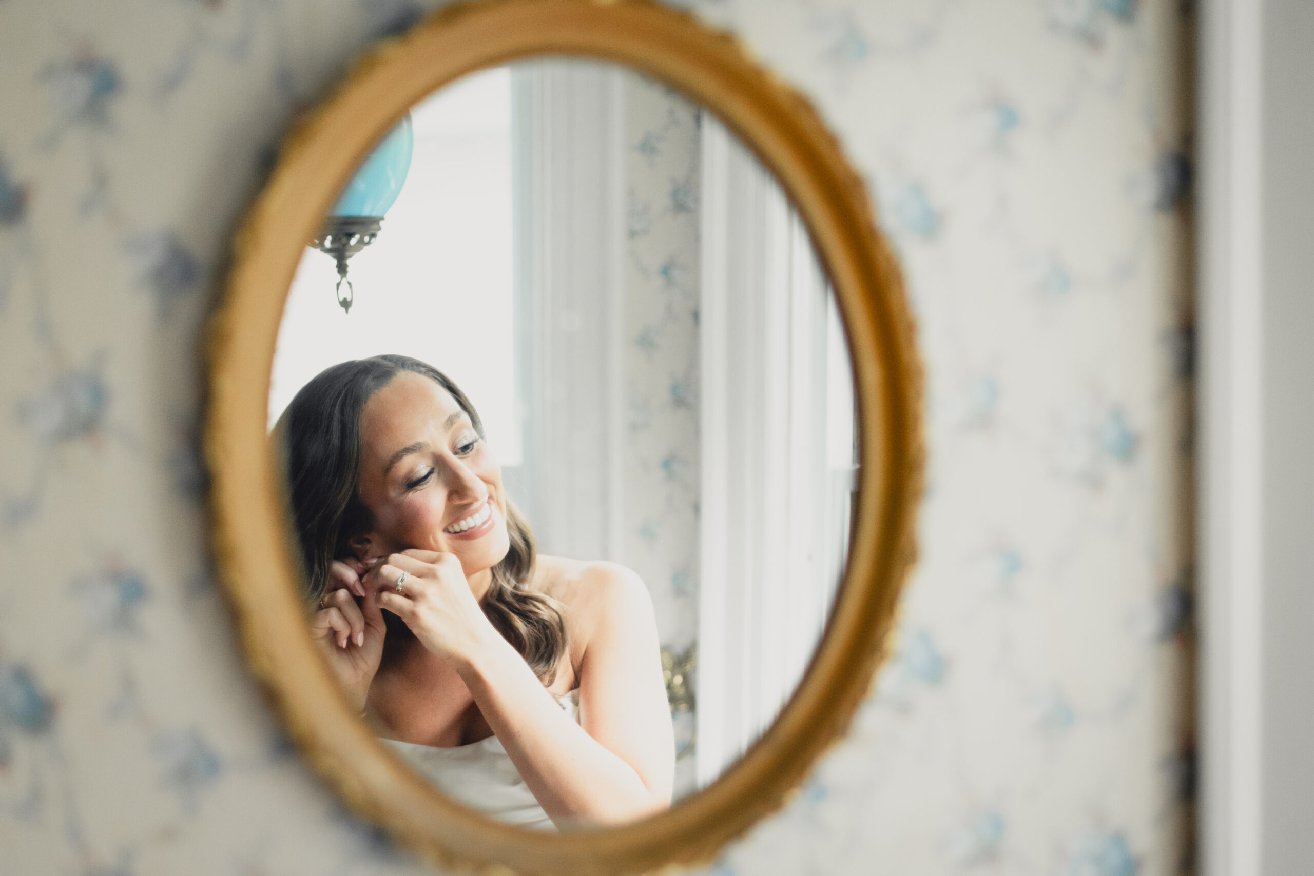 bride puts on earrings in mirror in childhood bedroom before wedding in Buffalo, NY
