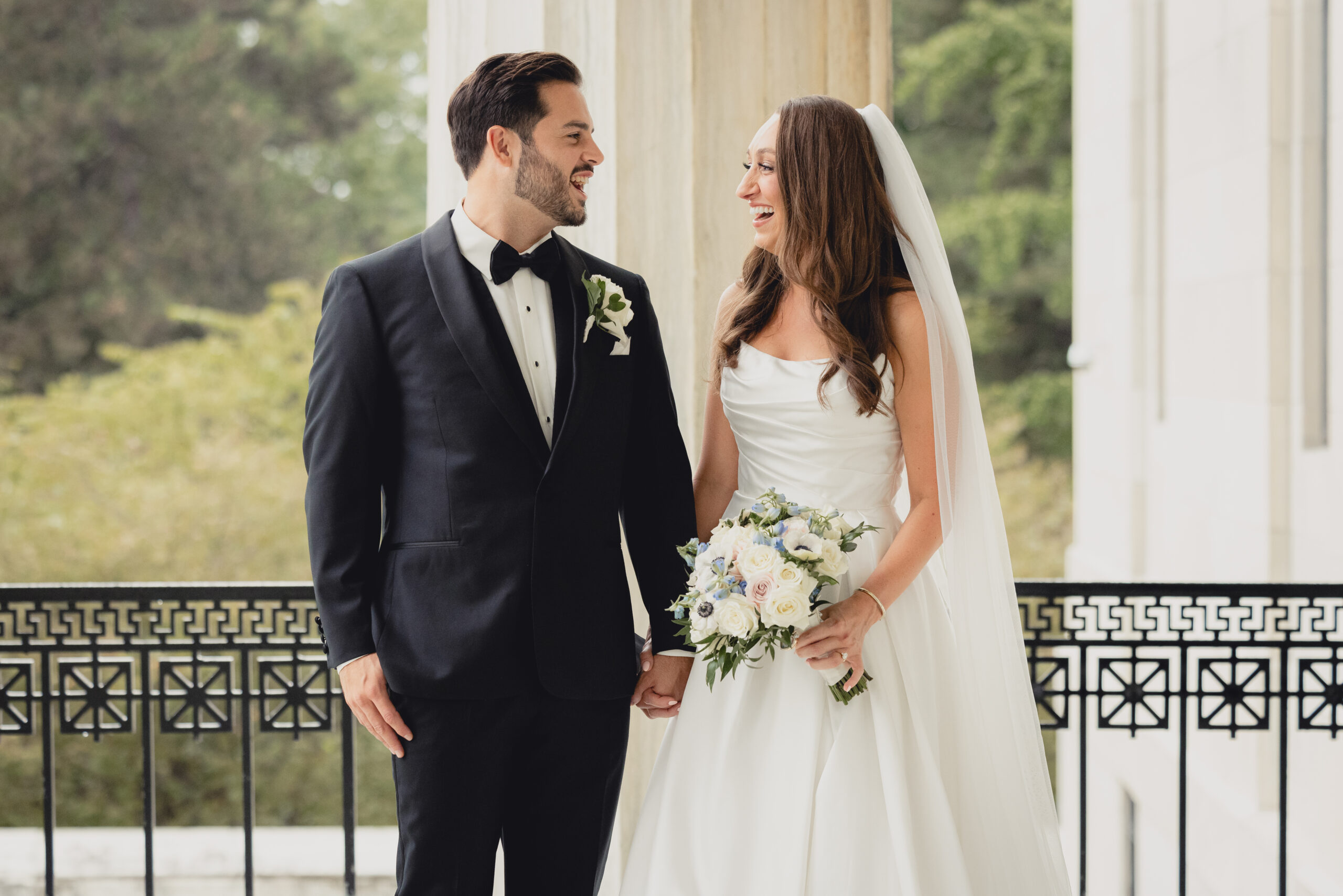 bride and groom hold hands and laugh on Portico of the Buffalo History Museum on wedding day