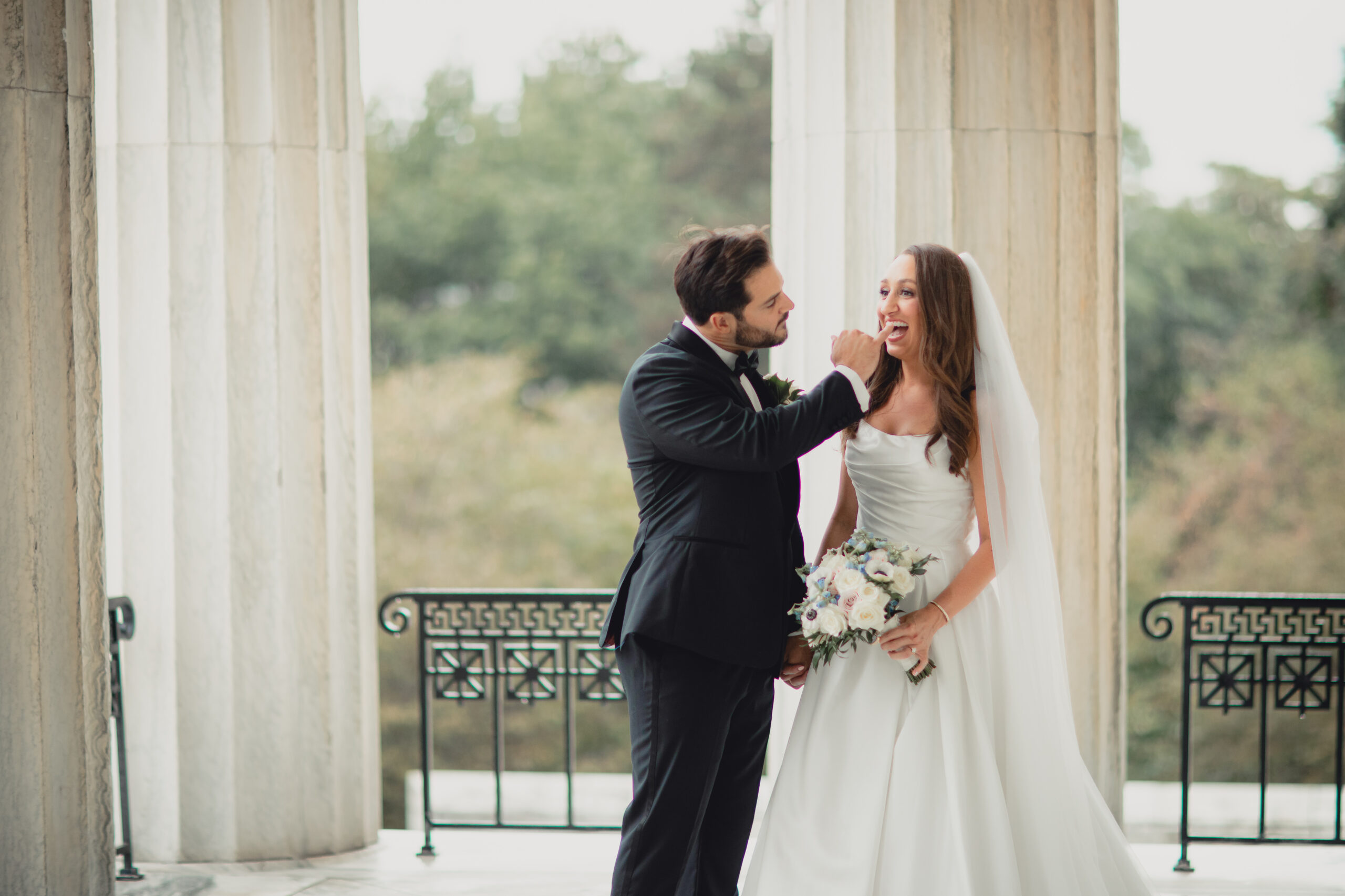 groom cleans brides teeth bride on portico of the Buffalo History Museum on wedding day