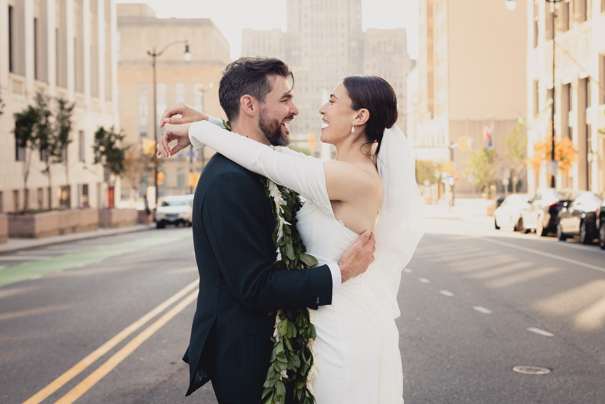 bride and groom laugh during portrait session in downtown Buffalo, NY with City Hall in background after wedding ceremony