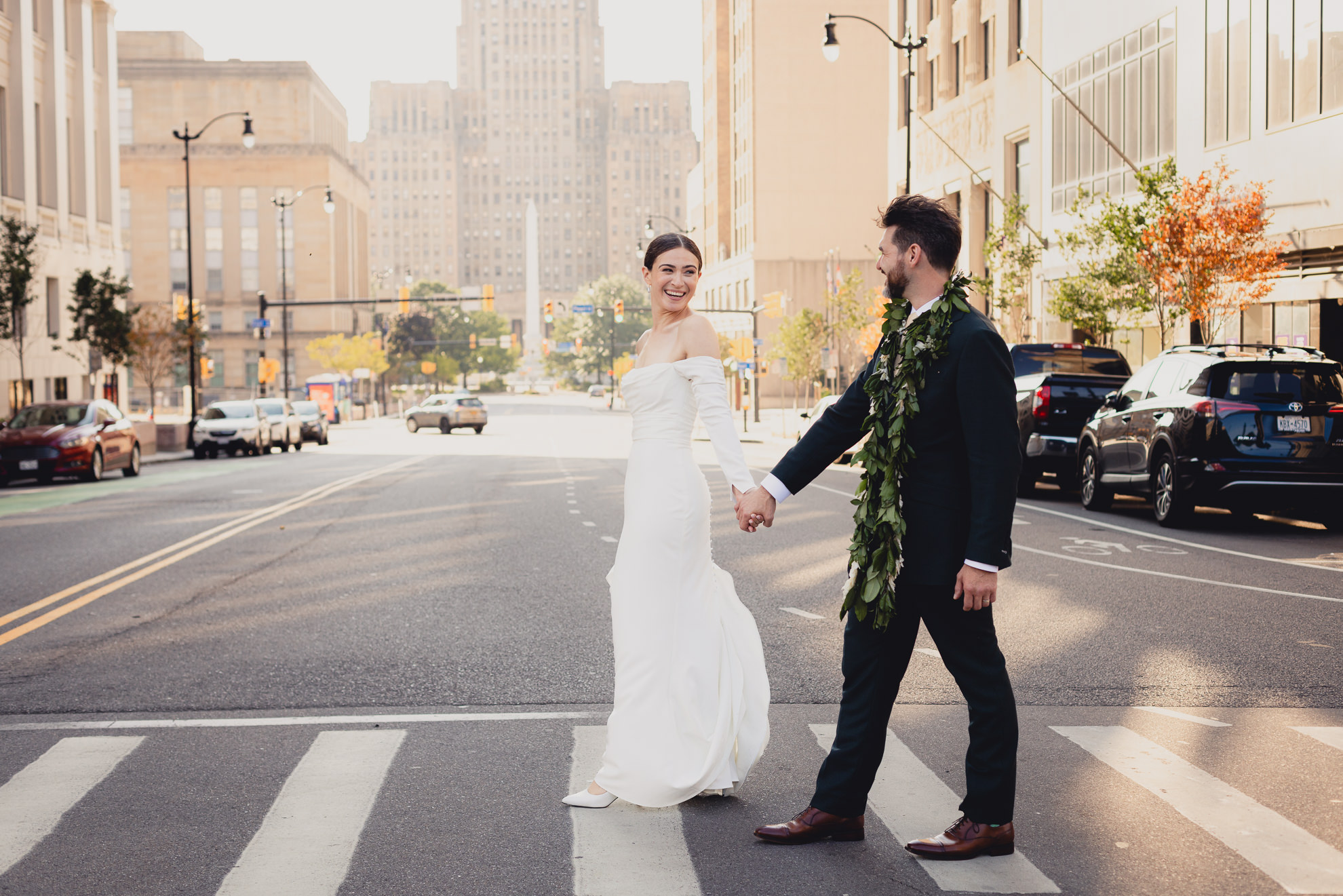 bride and groom cross street downtown Buffalo, NY with City Hall in background after wedding ceremony