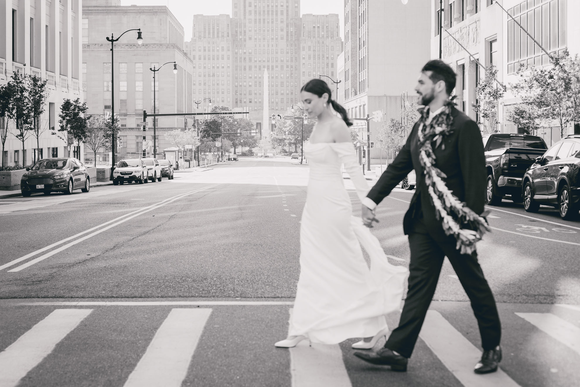 bride and groom cross street downtown Buffalo, NY with City Hall in background after wedding ceremony