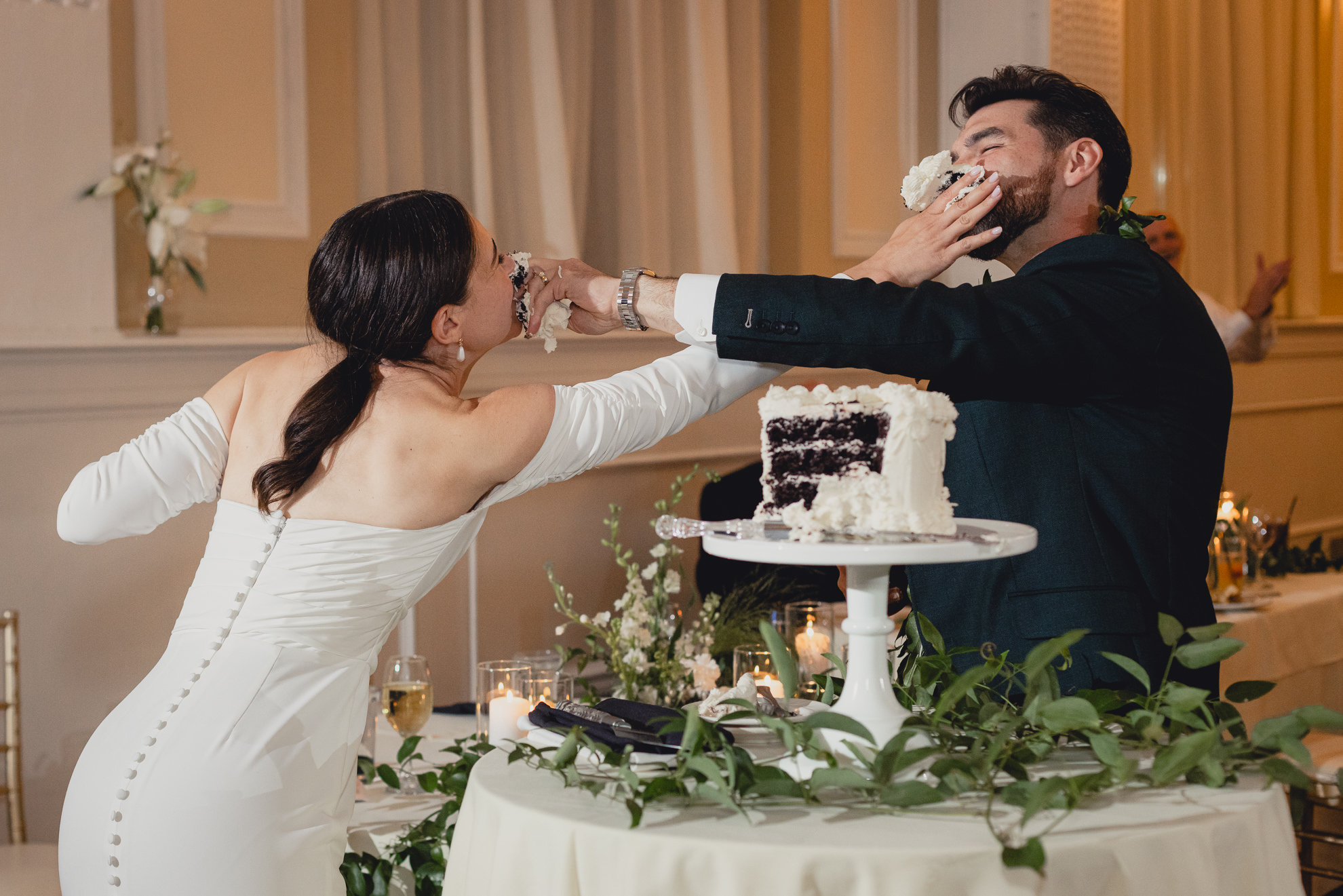 bride and groom shove cake all over each others faces during wedding reception at the Hotel Lafayette in Buffalo, NY