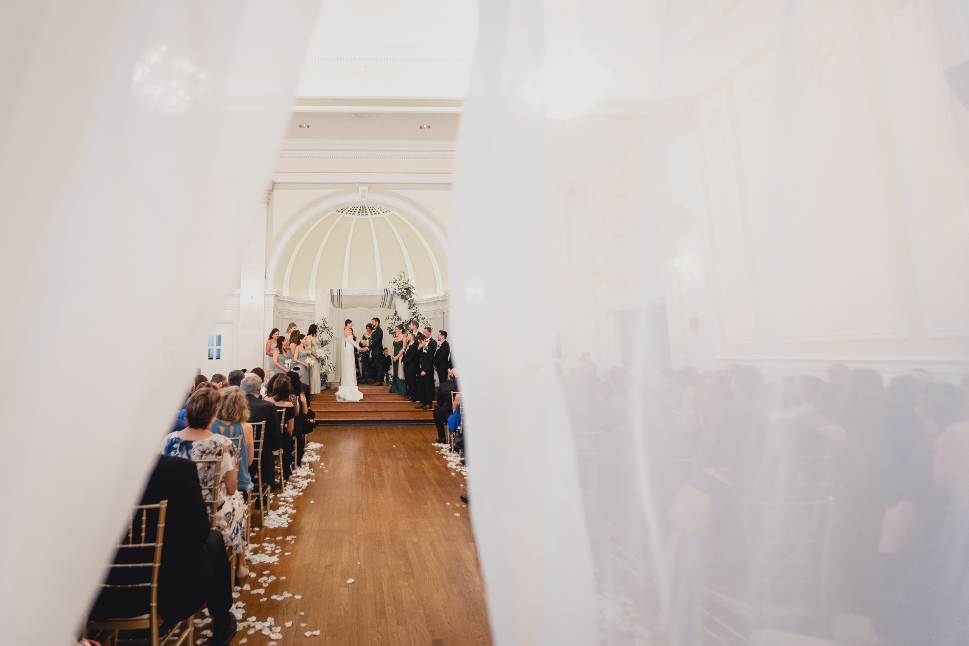 wedding ceremony seen from between sheer curtains in the Golden Ballroom of the Hotel Lafayette