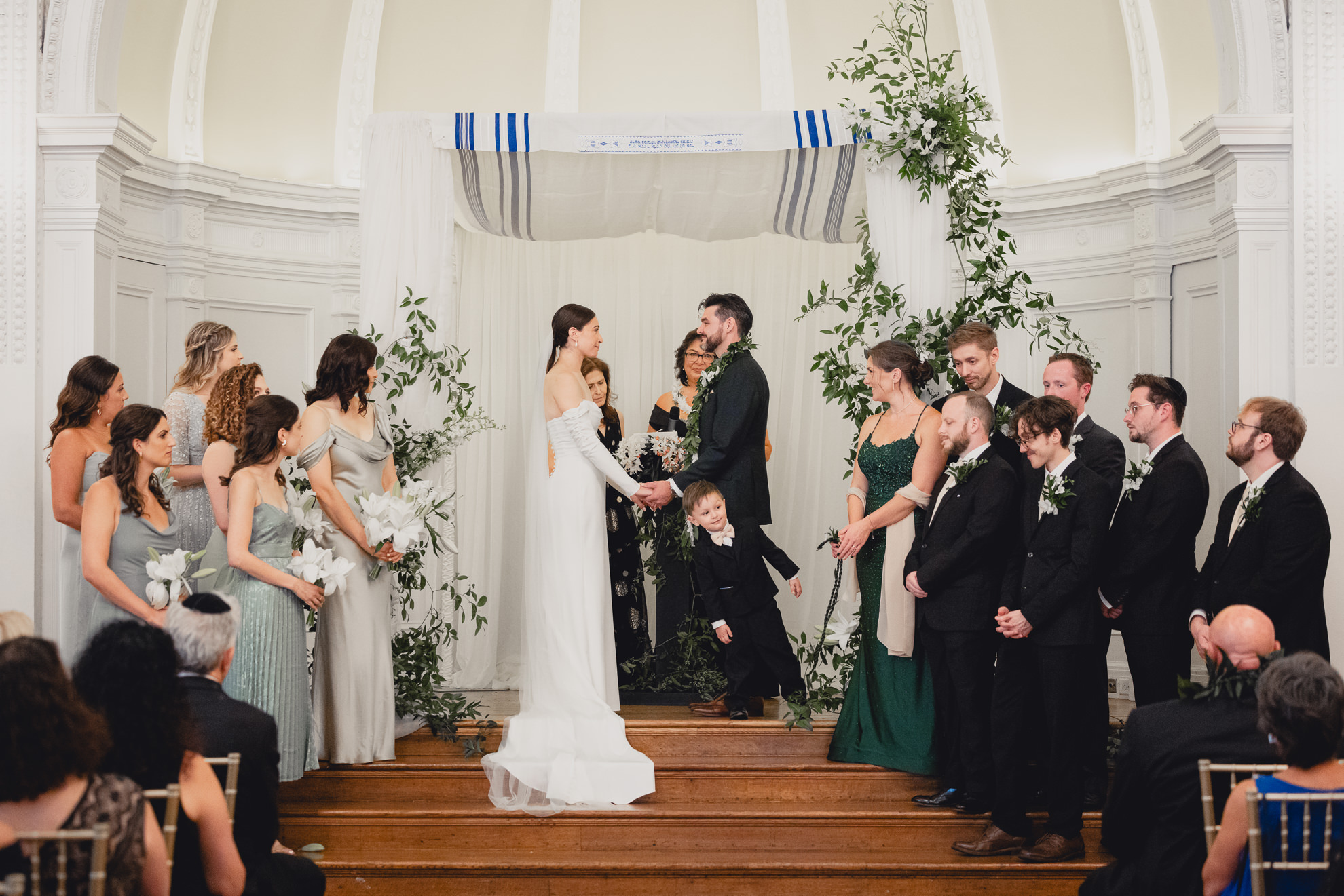 bride and groom hold hands while surrounded by wedding party on stage during wedding ceremony in the Golden Ballroom of the Hotel Lafayette