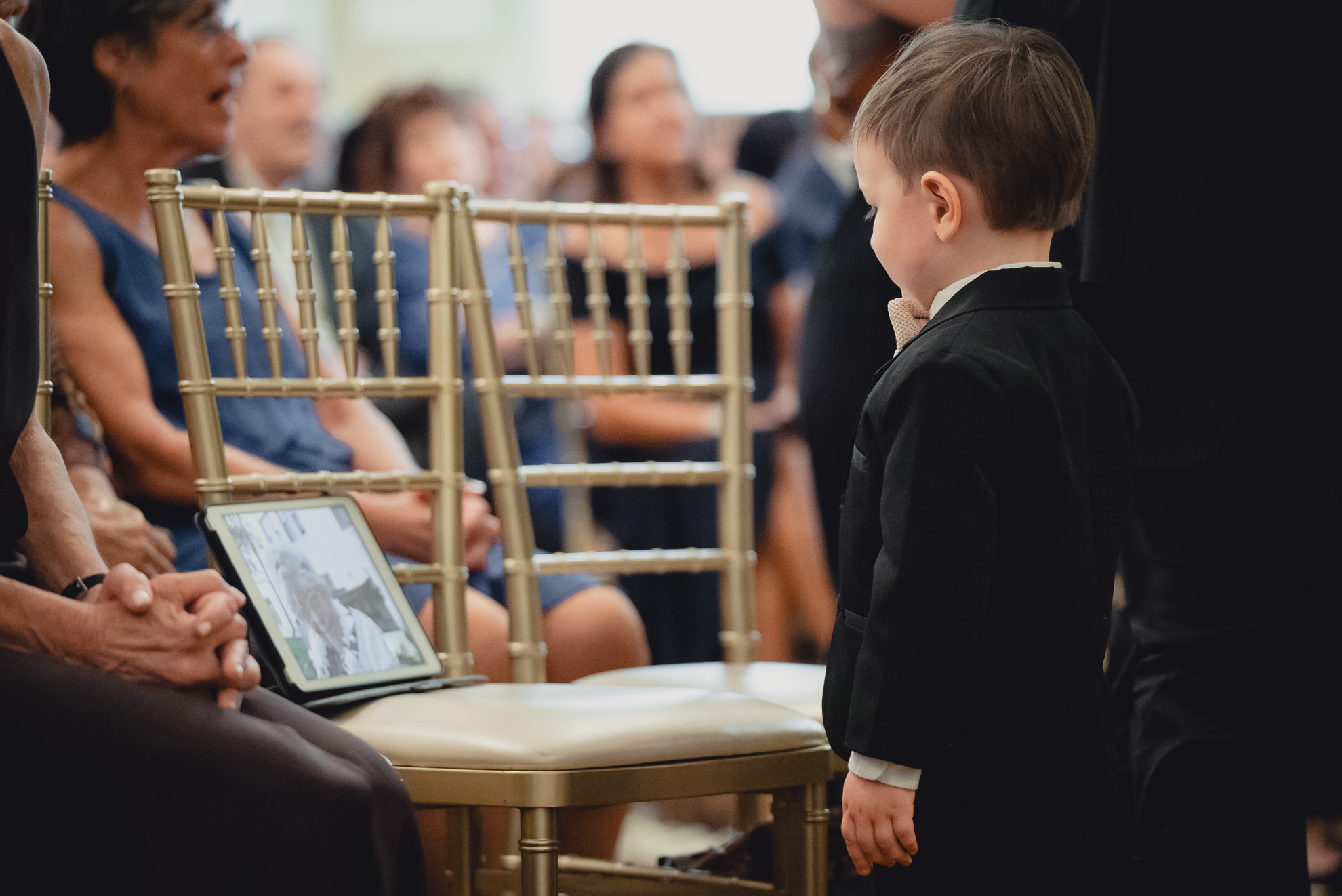 ring bearer looks at grandmother on tablet over Zoom during wedding ceremony in the Golden Ballroom of the Hotel Lafayette