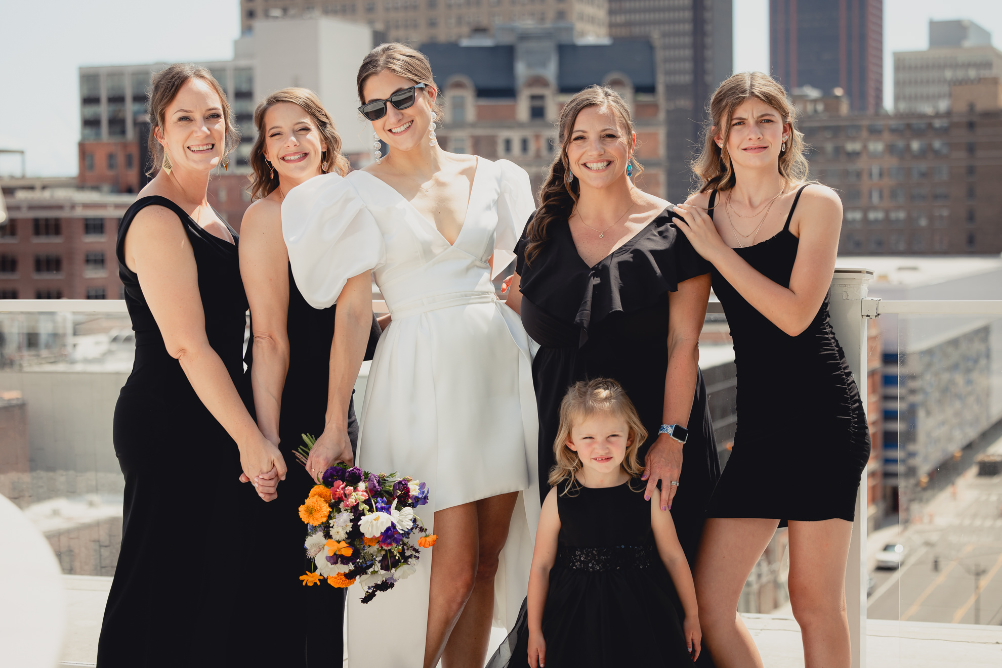 bride poses with bridesmaids with skyline in background before wedding at Vue on the roof of the Curtiss Hotel in Buffalo, NY