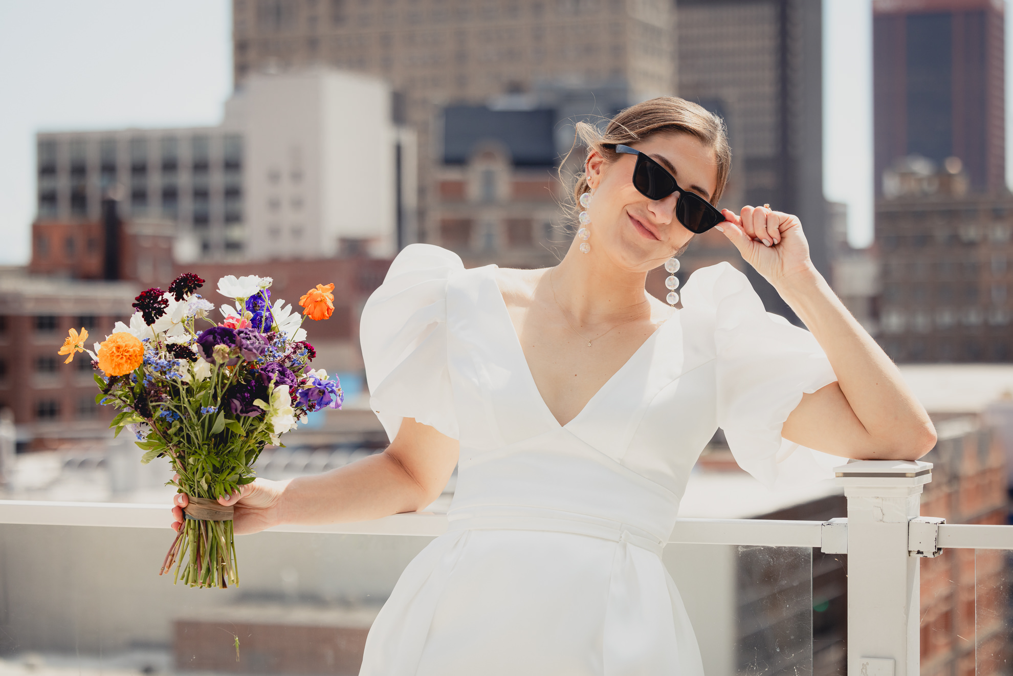 bride poses with sunglasses with skyline in background before wedding at Vue on the roof of the Curtiss Hotel in Buffalo, NY