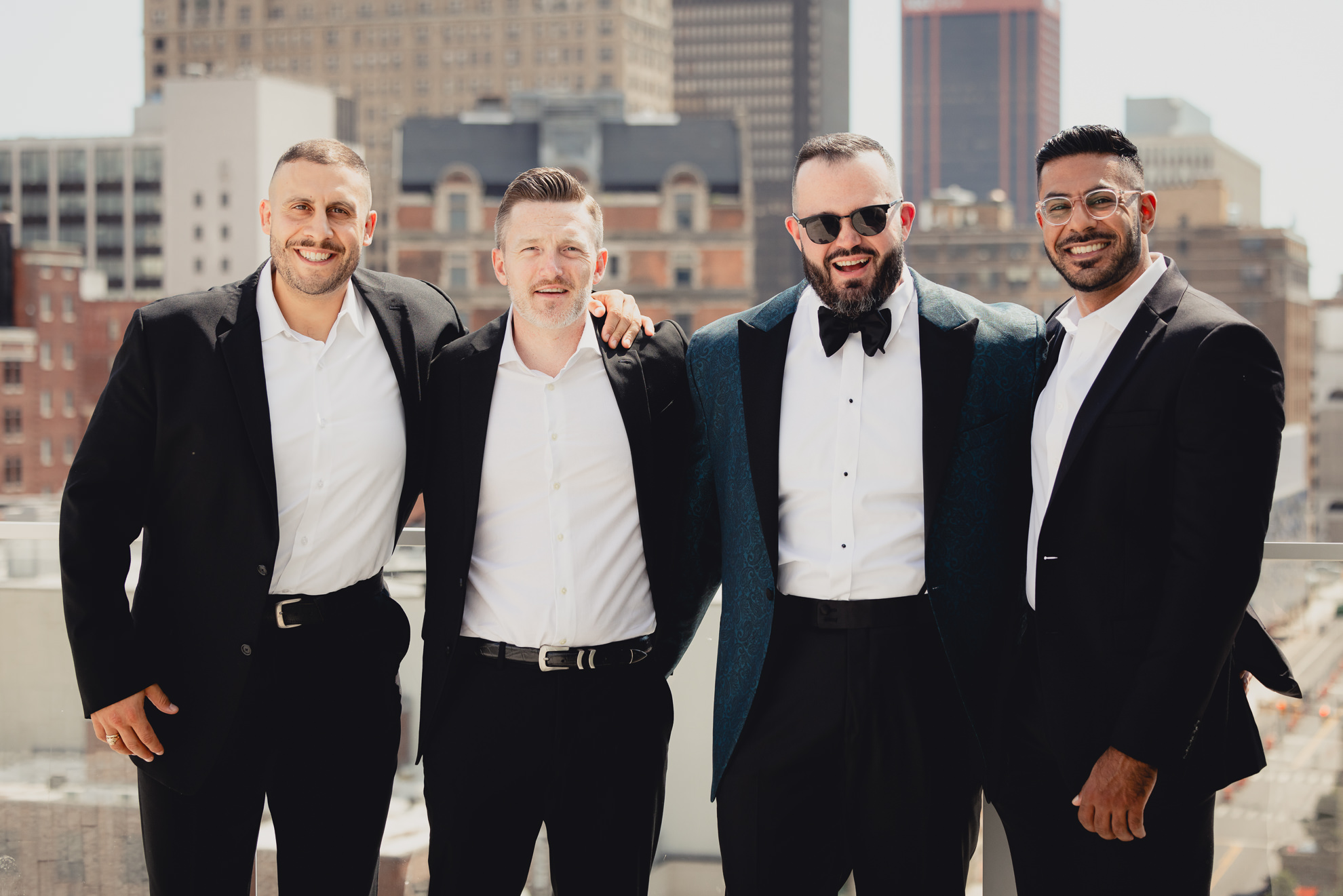 groom poses with groomsmen with skyline in background before wedding at Vue on the roof of the Curtiss Hotel in Buffalo, NY