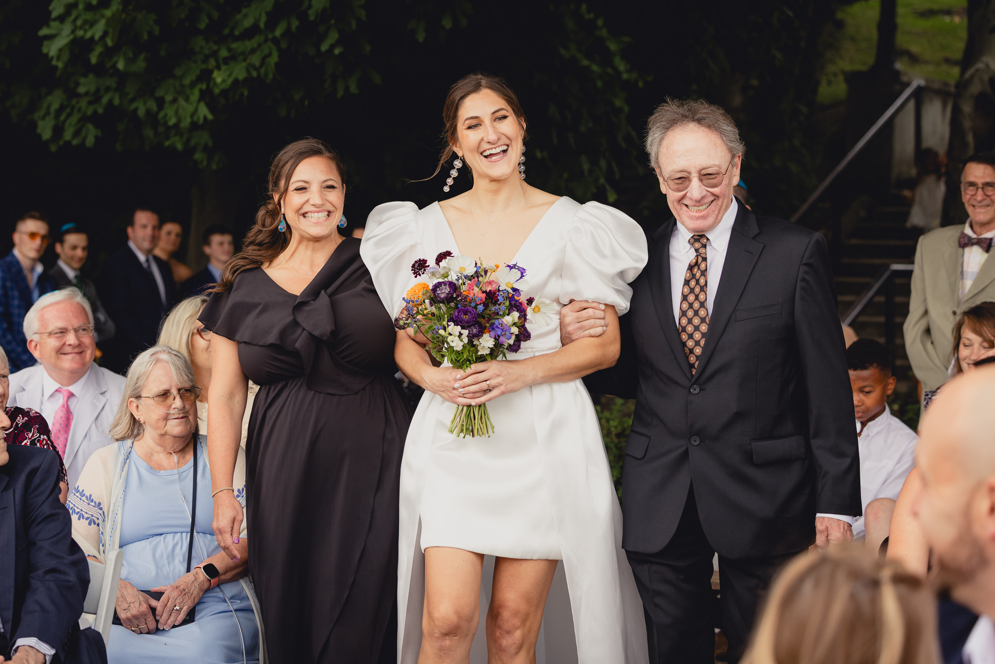 bride is escorted down aisle by father and sister during wedding ceremony at Hoyt Lake at the Terrace at Marcy Casino in Buffalo