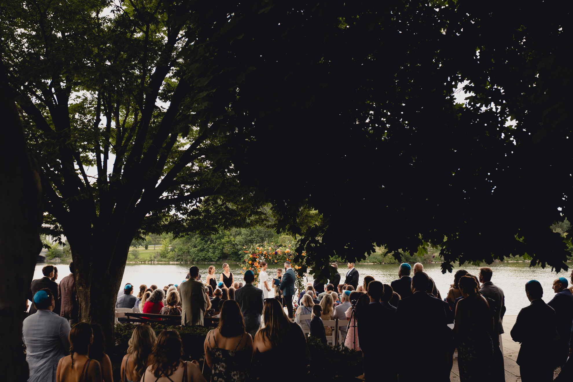 wedding ceremony seen through trees at Hoyt Lake at the Terrace at Marcy Casino in Buffalo, NY