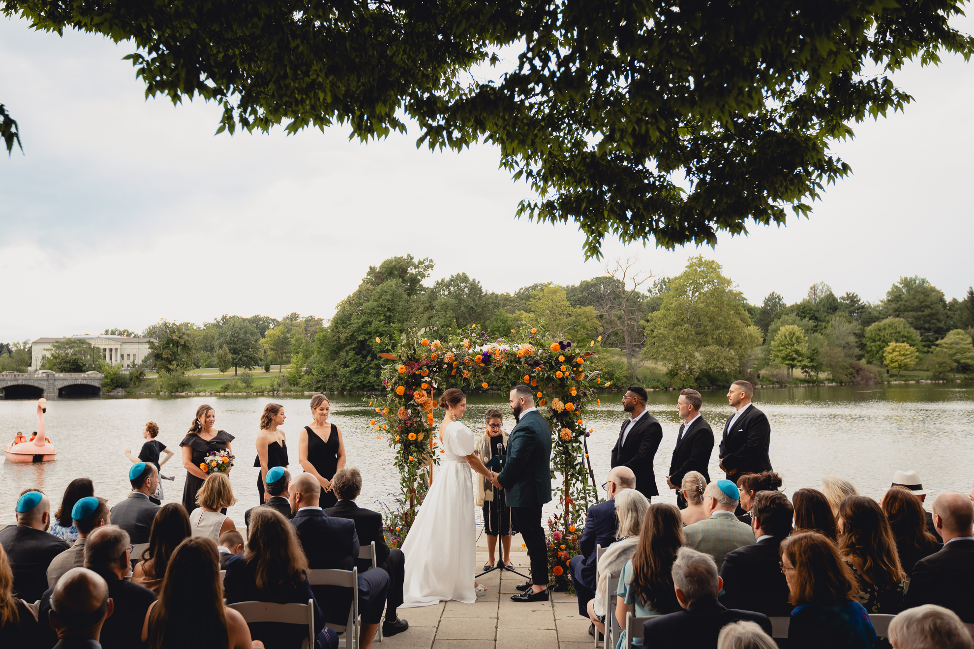 bride and groom hold hands and gaze at one another during wedding ceremony at Hoyt Lake at the Terrace at Marcy Casino in Buffalo, NY