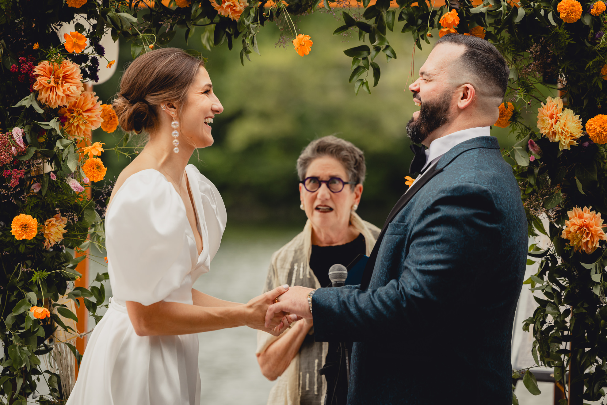 bride and groom hold hands and laugh together during wedding ceremony at Hoyt Lake at the Terrace at Marcy Casino in Buffalo, NY