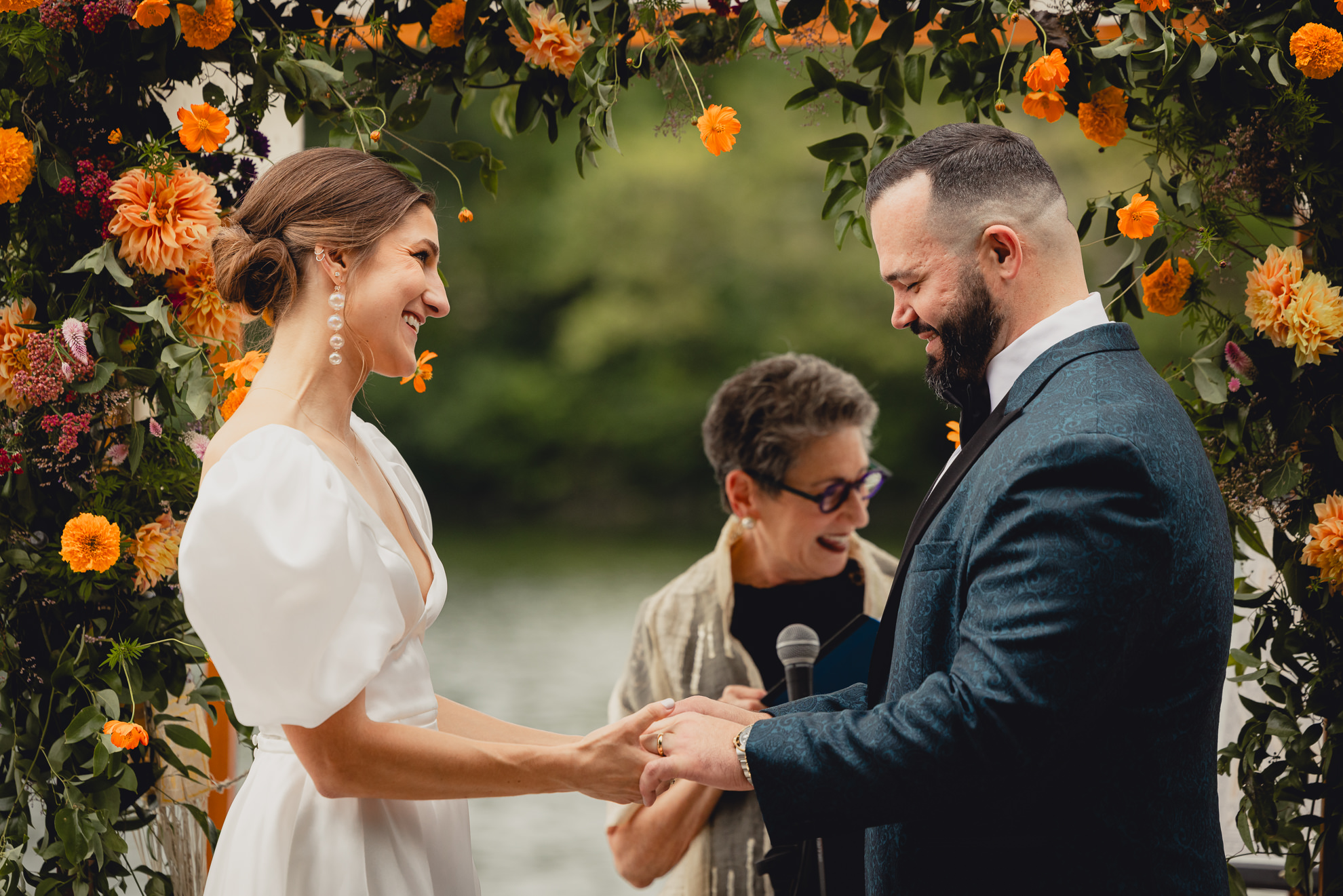 bride and groom hold hands and laugh together during wedding ceremony at Hoyt Lake at the Terrace at Marcy Casino in Buffalo, NY