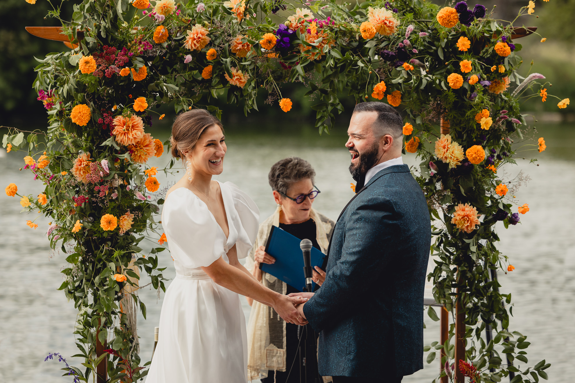 bride and groom hold hands and laugh together during wedding ceremony at Hoyt Lake at the Terrace at Marcy Casino in Buffalo, NY