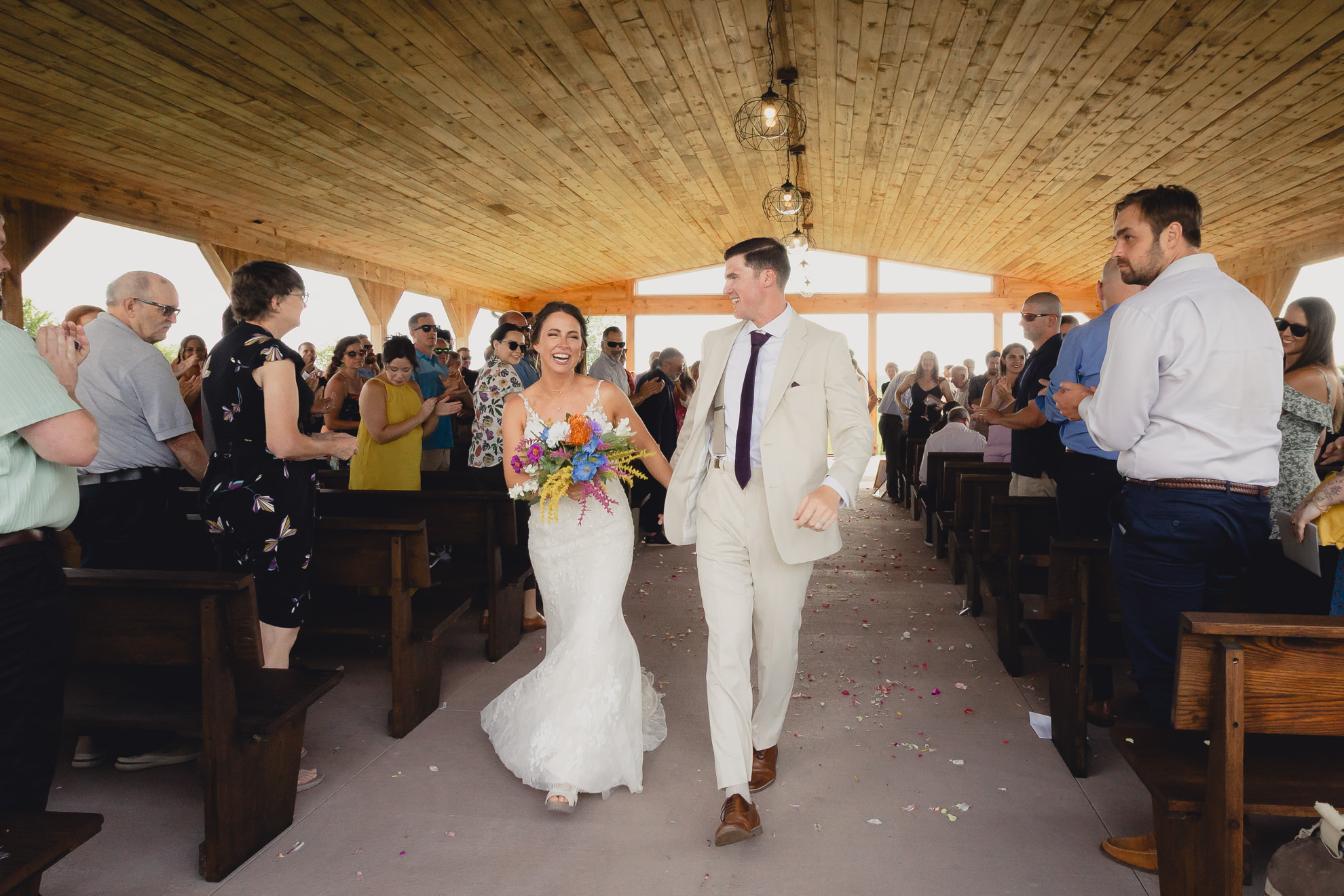 bride and groom laugh while walking up aisle during wedding ceremony at The Gallagher Barn in Medina, NY